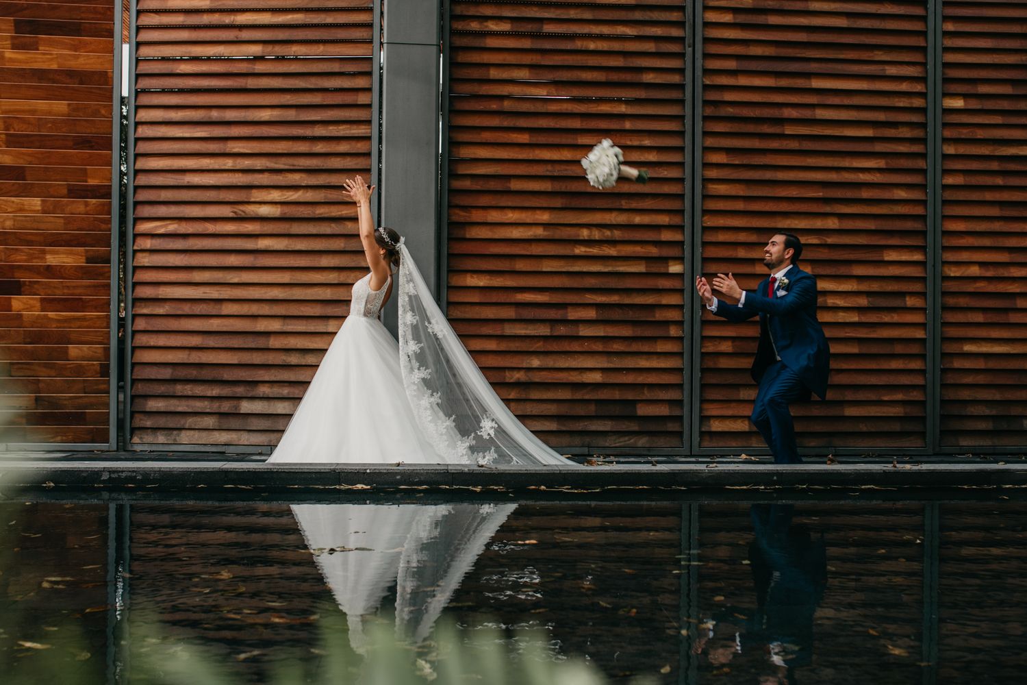 Wedding couple reflected in still water by wooden wall creating mirror image.
