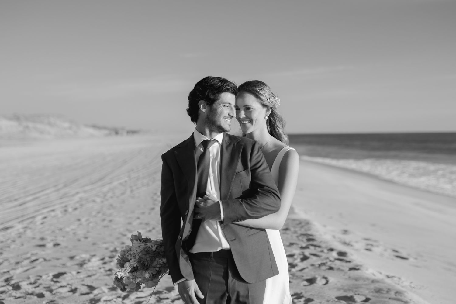 A black and white beach wedding portrait capturing an intimate moment on the sand.