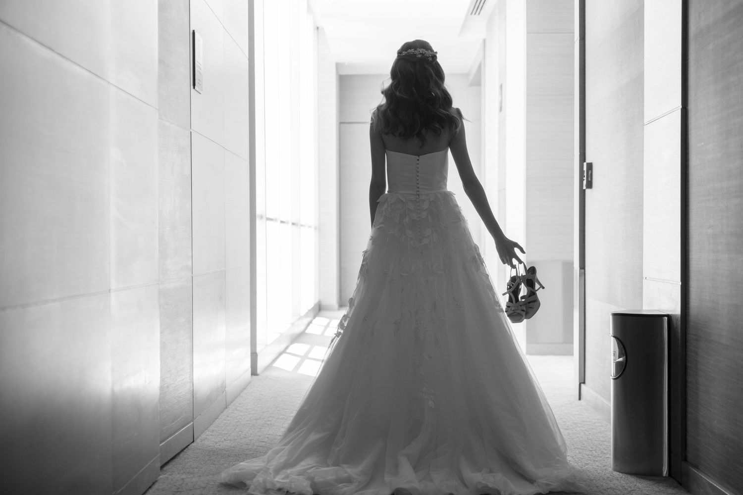 A silhouette of a bride in a flowing wedding gown standing in a sunlit hallway.