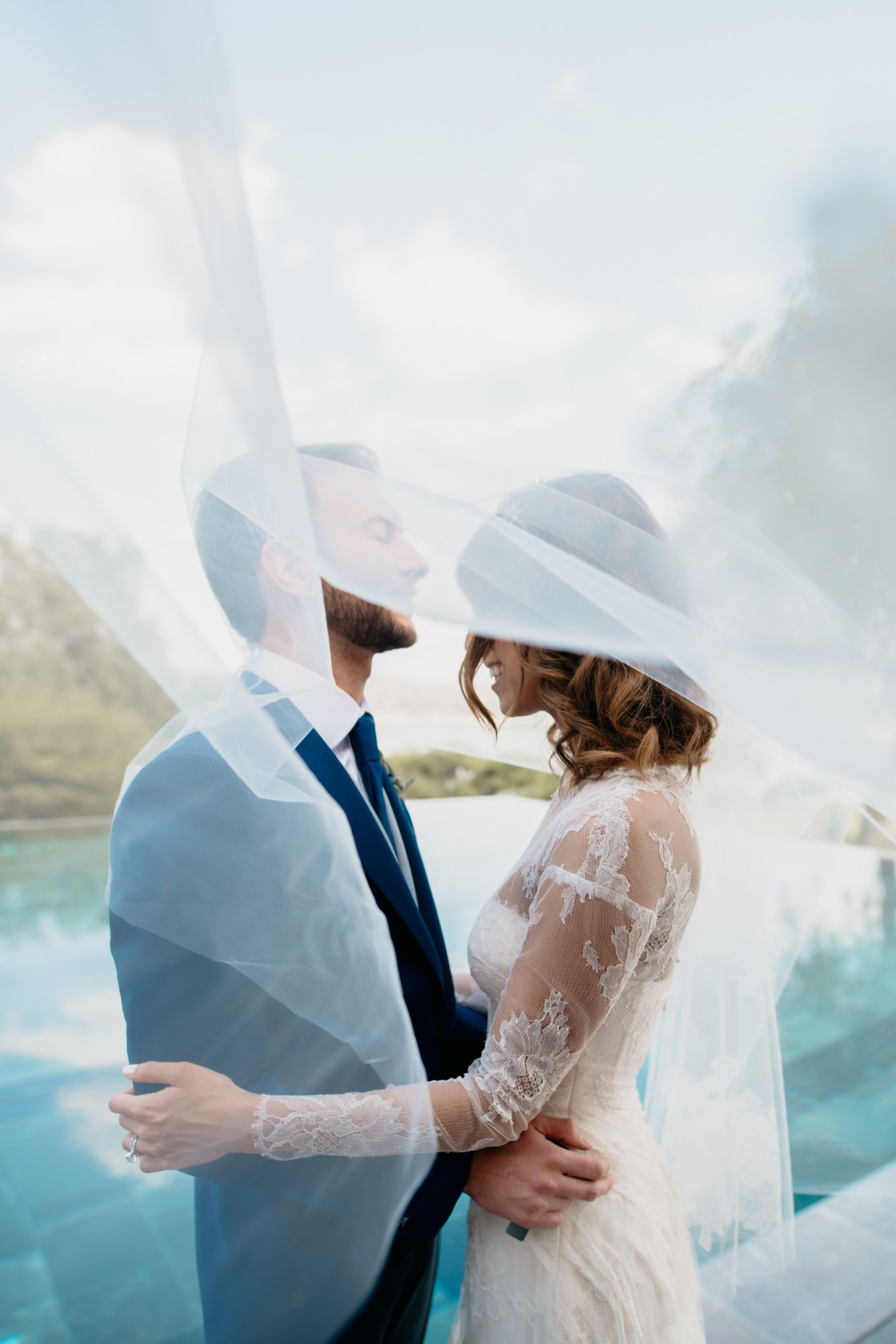 Ethereal mountain wedding portrait with bride and groom embracing under flowing veil.