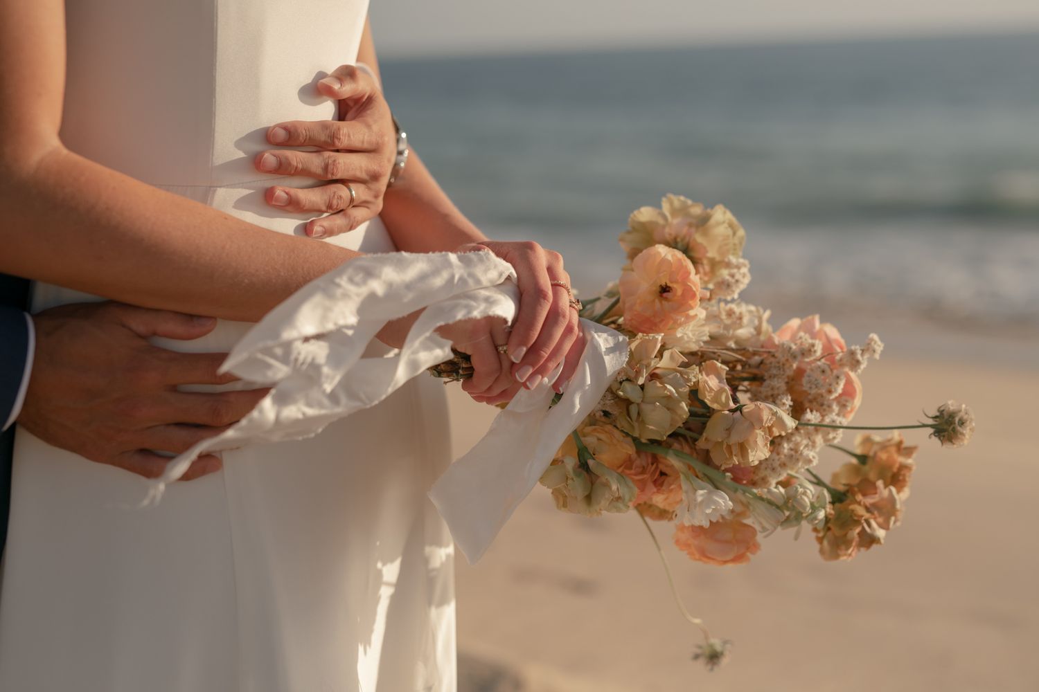 Delicate dried flower bouquet held against a white dress with ocean waves in the background.