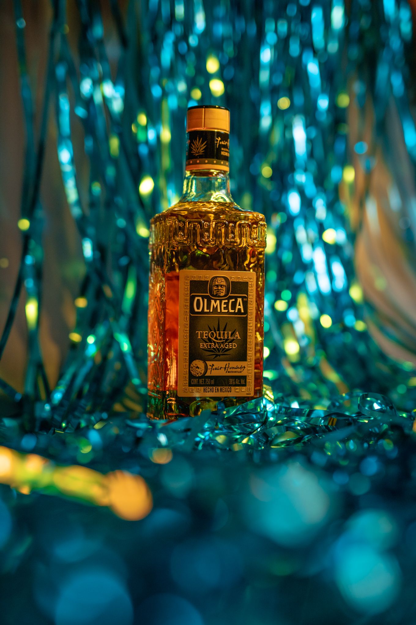 Olmeca tequila bottle displayed with glowing blue and gold bokeh backdrop.