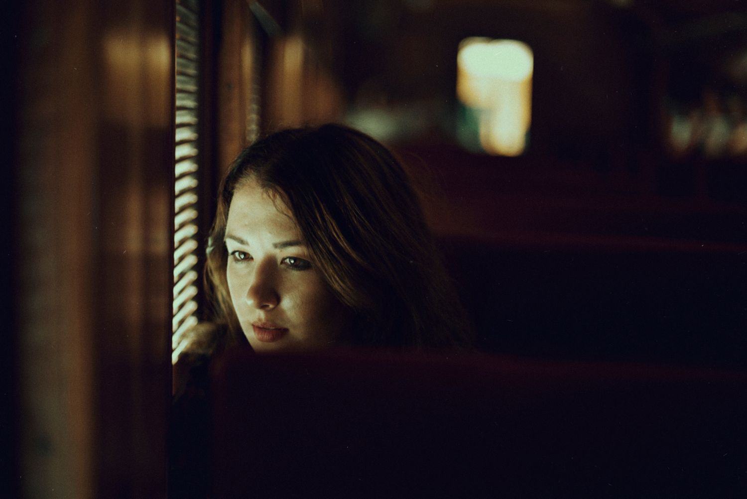 Dark atmospheric photo of someone looking out window in dim lighting.
