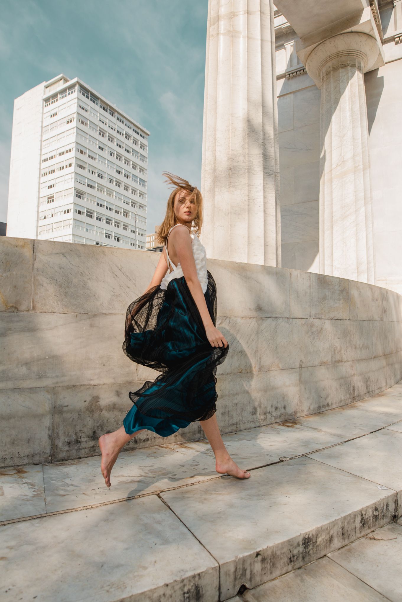 Candid fashion shot of someone in flowing blue dress on white marble steps near modern building.