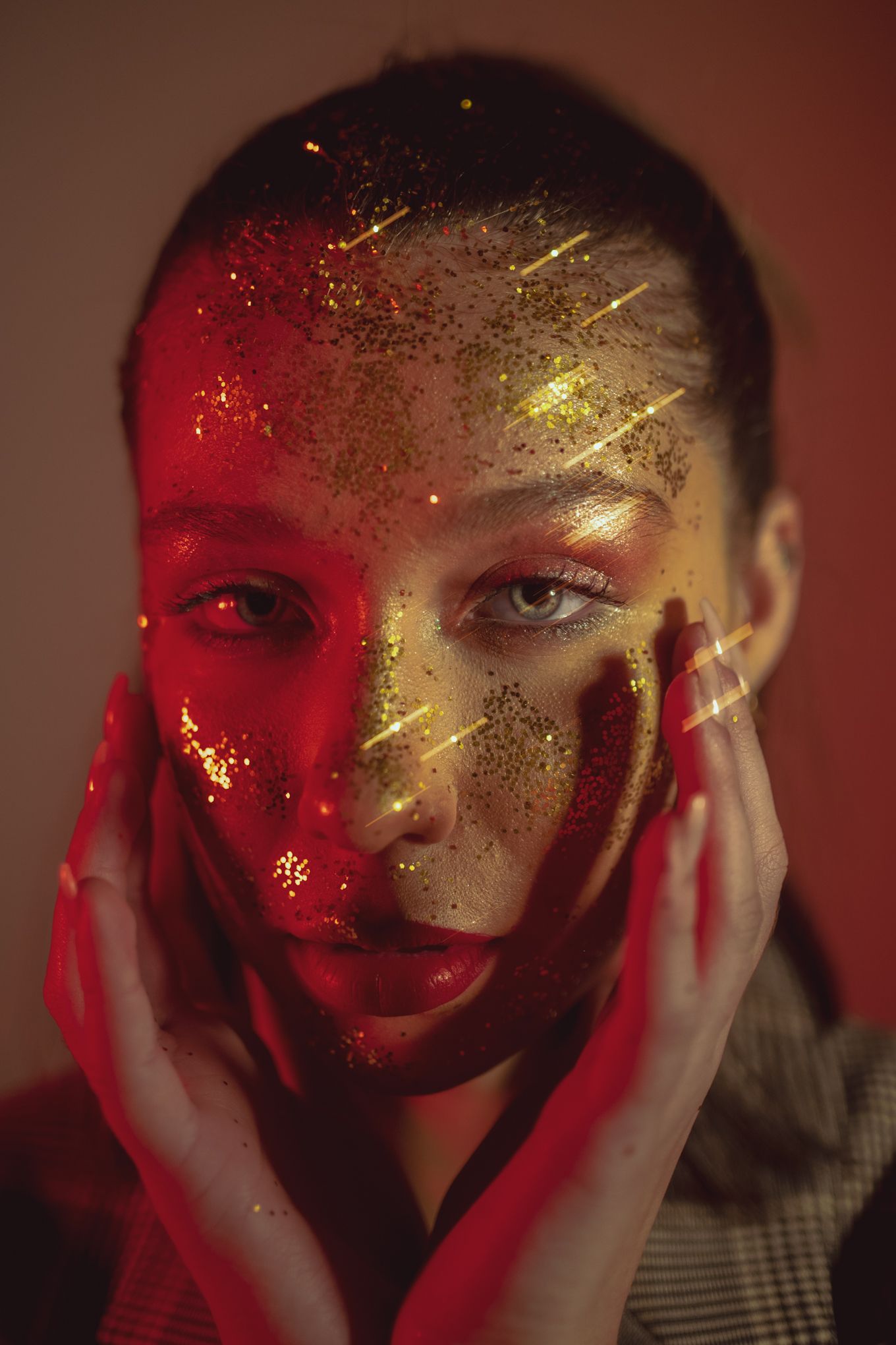 Creative beauty portrait with gold glitter and red lighting creating dramatic contrast.