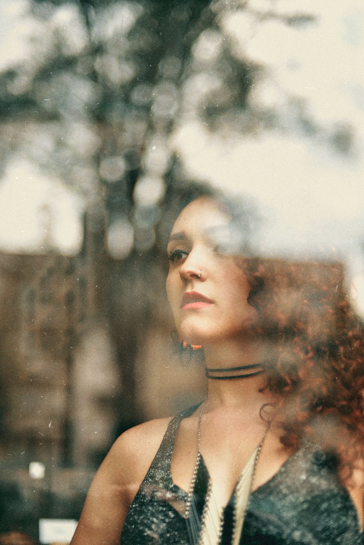 Dreamy portrait through glass with bokeh effects and choker necklace.