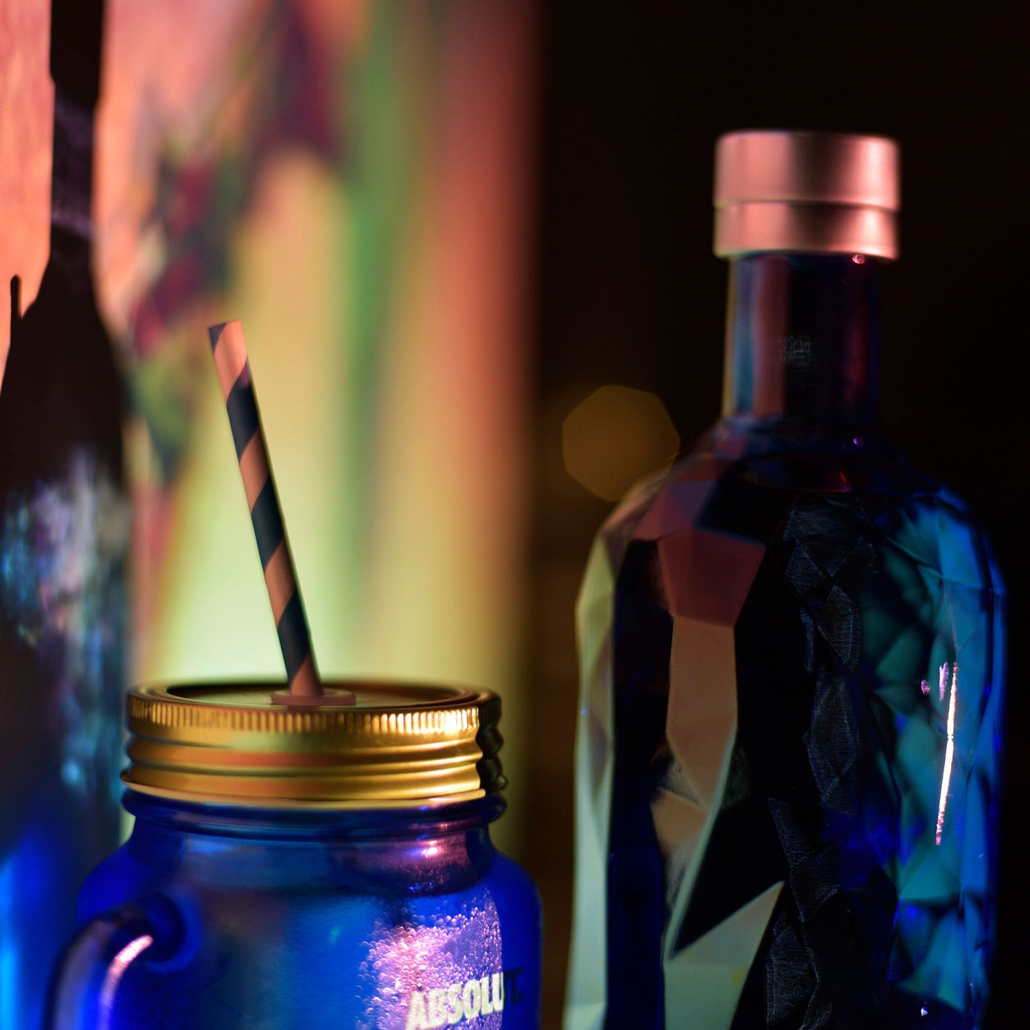 Colorful close-up shot of illuminated bottles in a bar with glowing pink and orange ambient lighting.