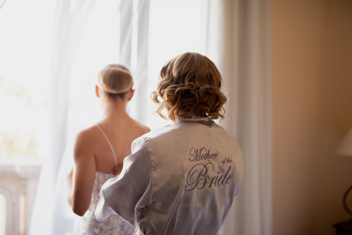 View from behind of two people in white robes near window, one with 