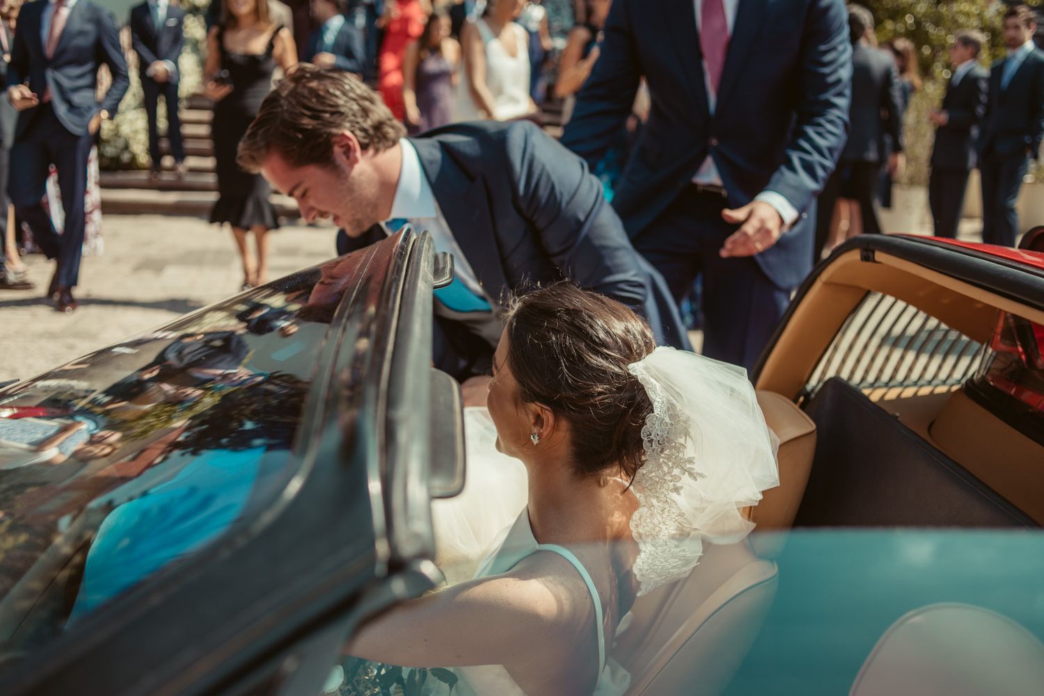 Newlyweds entering a classic car after their wedding ceremony with guests in background.