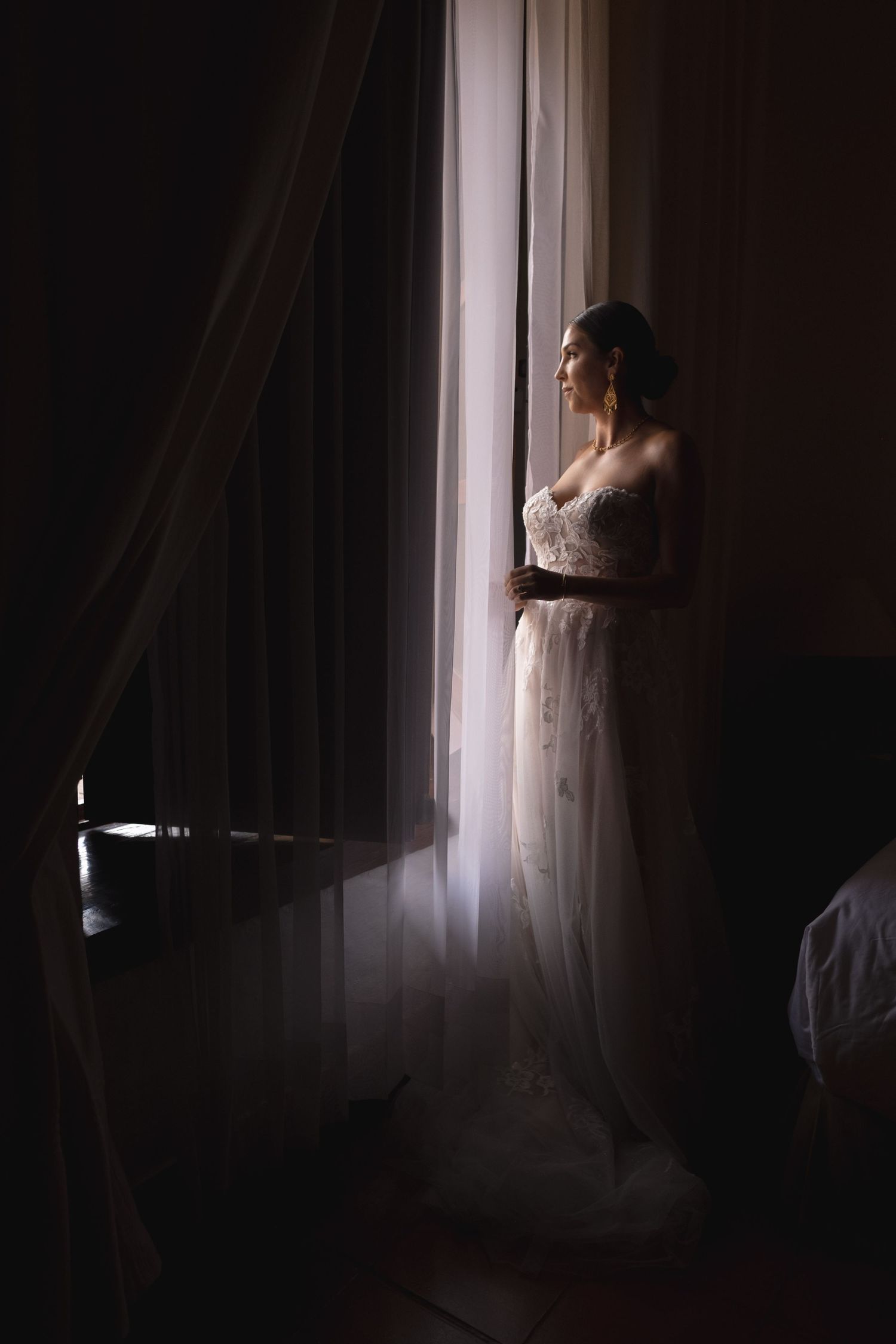 A silhouetted figure in a wedding dress gazes through a sunlit window.