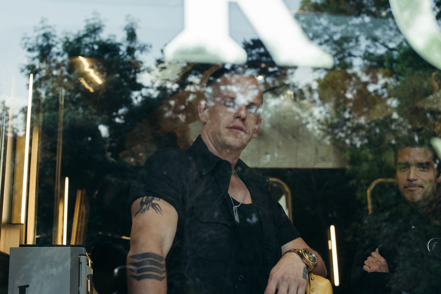 Candid shot through window showing person in black sleeveless shirt with tattoos.