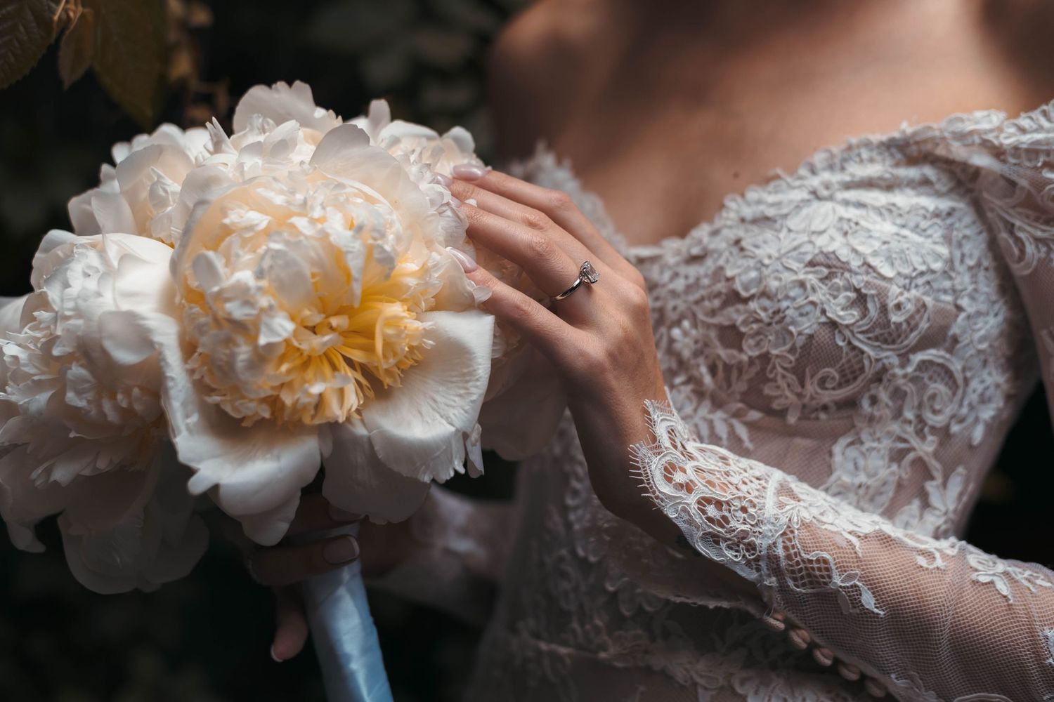 Close-up detail of white peony bouquet against intricate lace wedding dress.