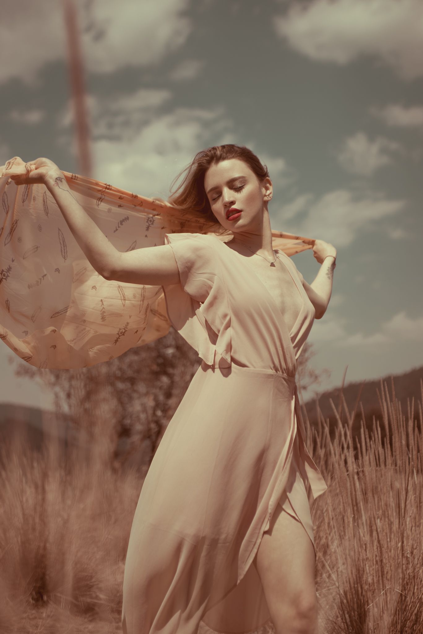 Woman in vintage dress poses gracefully in sun-lit field.