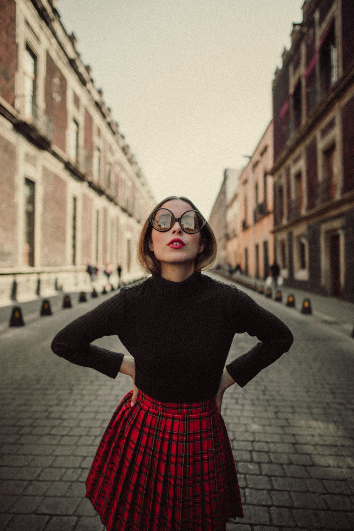 Street fashion photo featuring black turtleneck, red pleated skirt and cat-eye sunglasses.