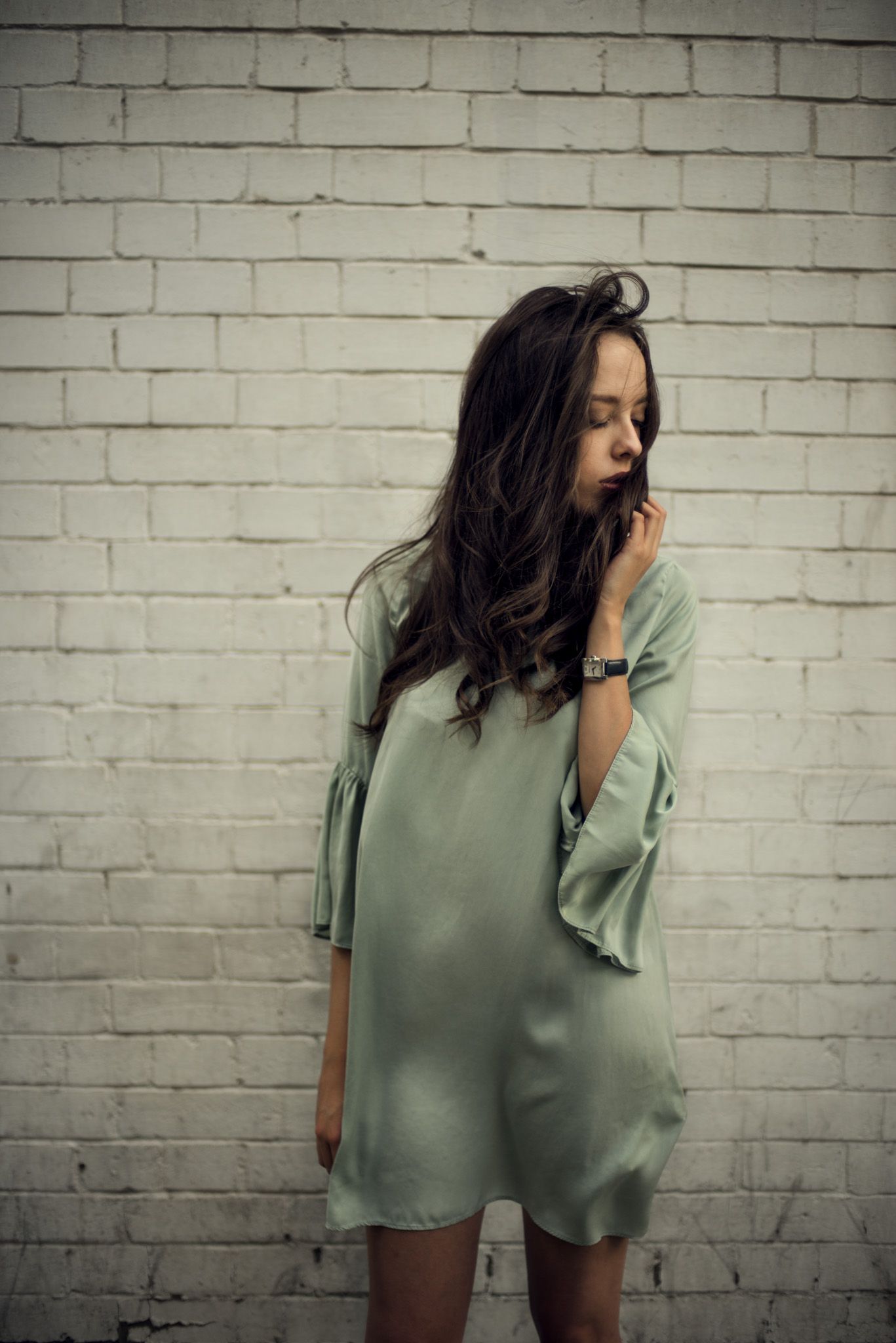 Fashion portrait in mint green dress against white brick wall.