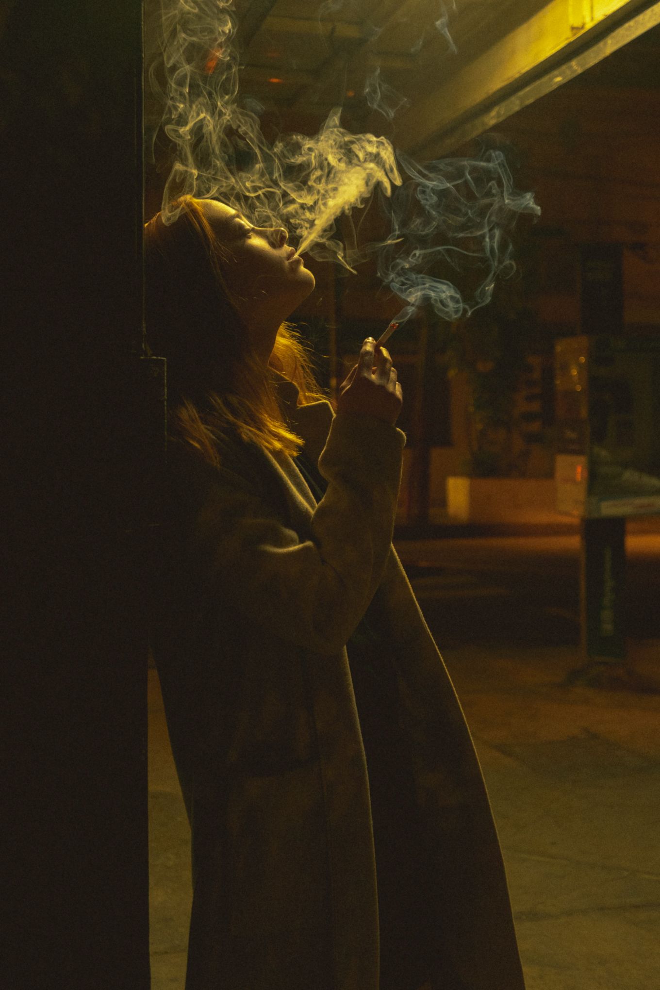 Dramatic silhouette exhaling smoke in dark amber-lit environment.