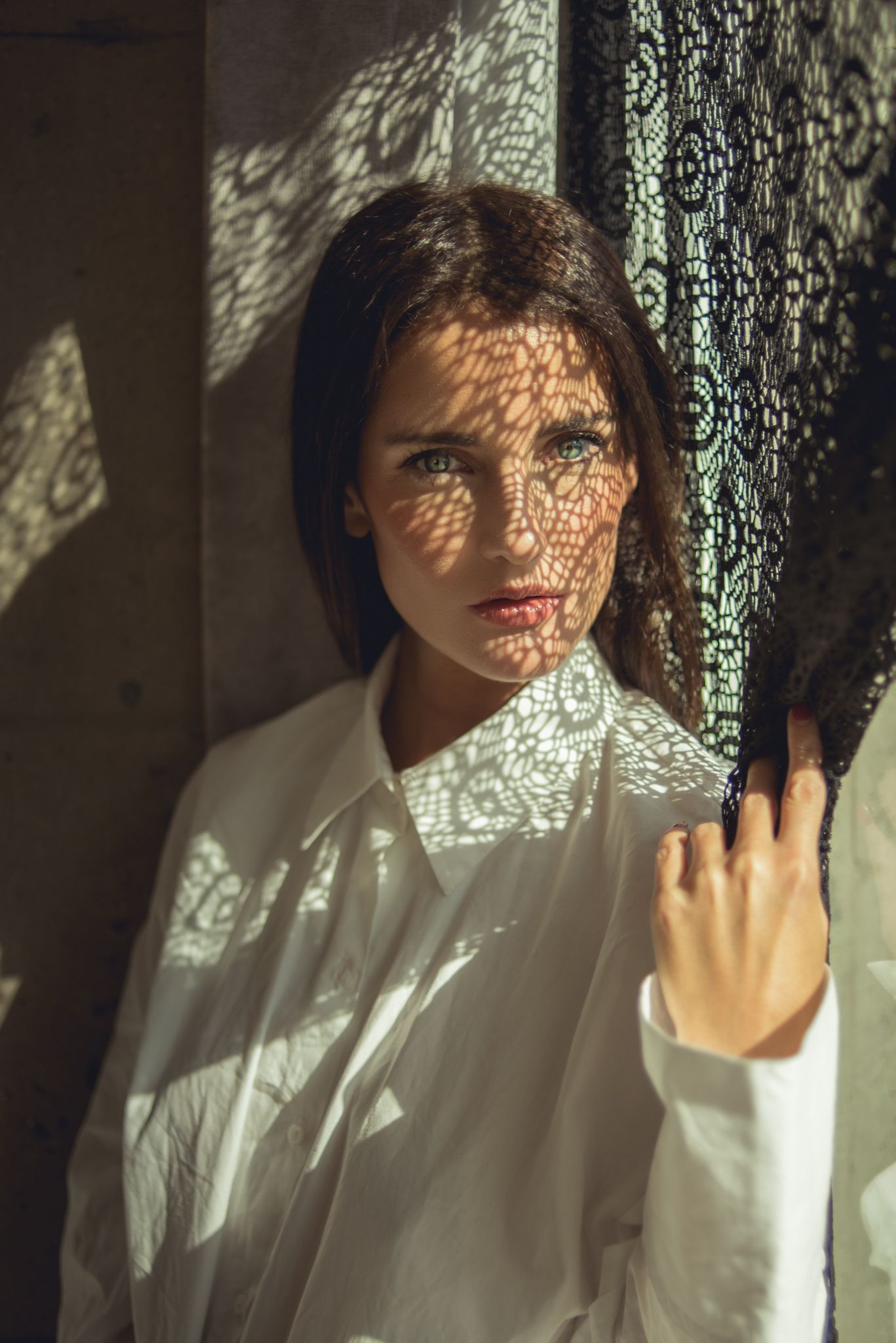 Artistic portrait with lace shadow patterns on face in natural light.