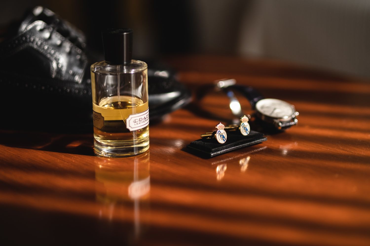 A glass of whiskey sits on a wooden table alongside watch and keys in dramatic lighting.