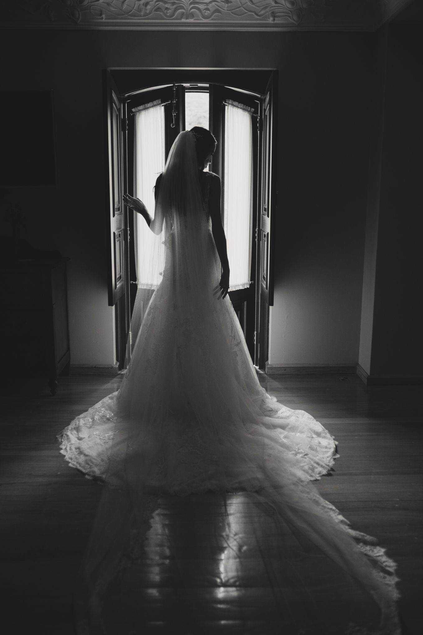 Dramatic black and white silhouette of a bride in flowing wedding dress standing in backlit doorway.