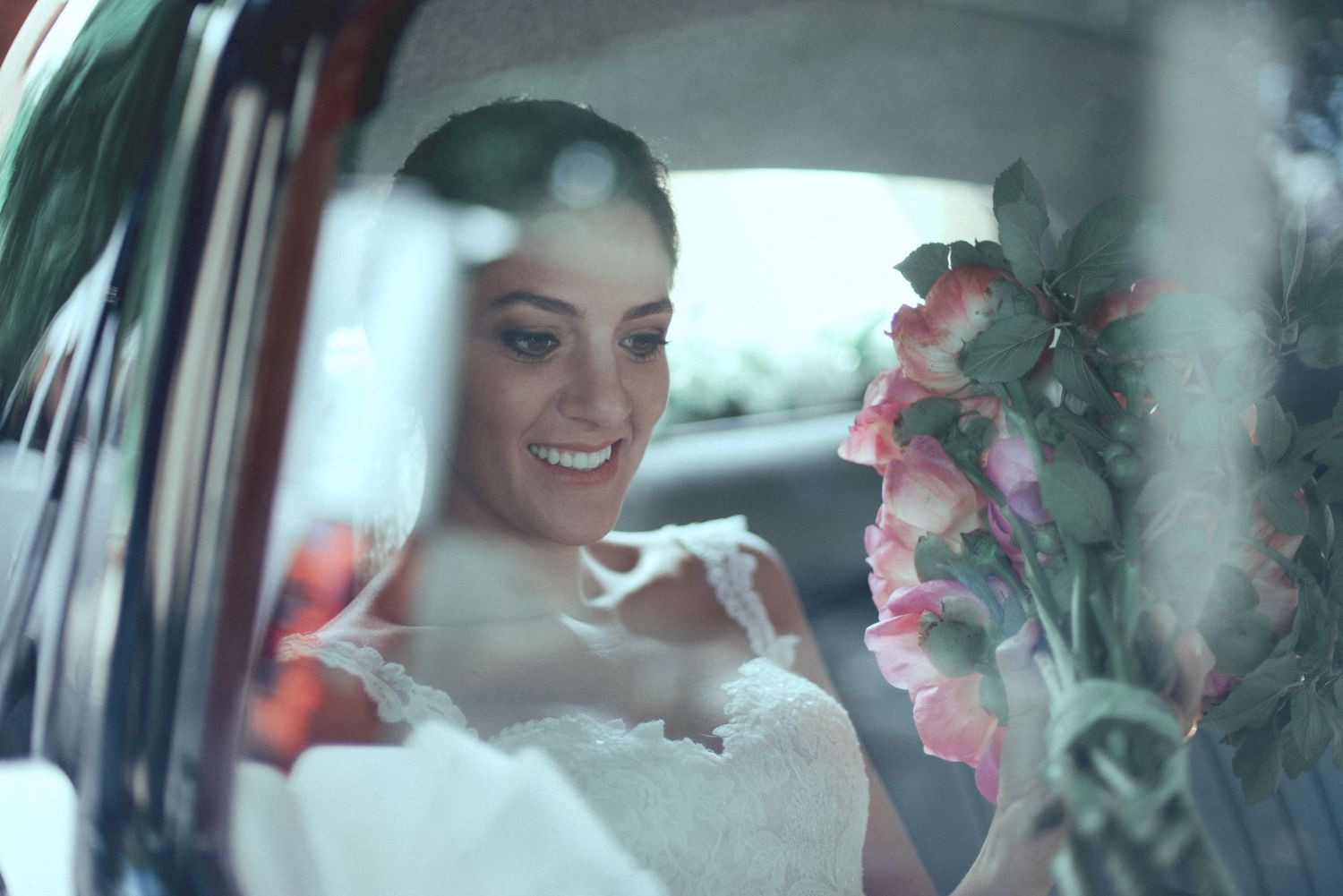 A bride sits in a car with pink flowers on a dreamy, soft focus wedding day.