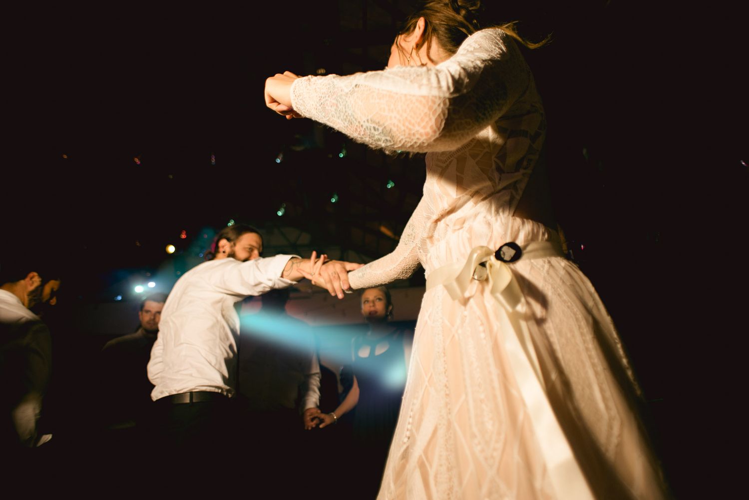 A couple spins and dances together during their wedding celebration at night with light effects in the background.
