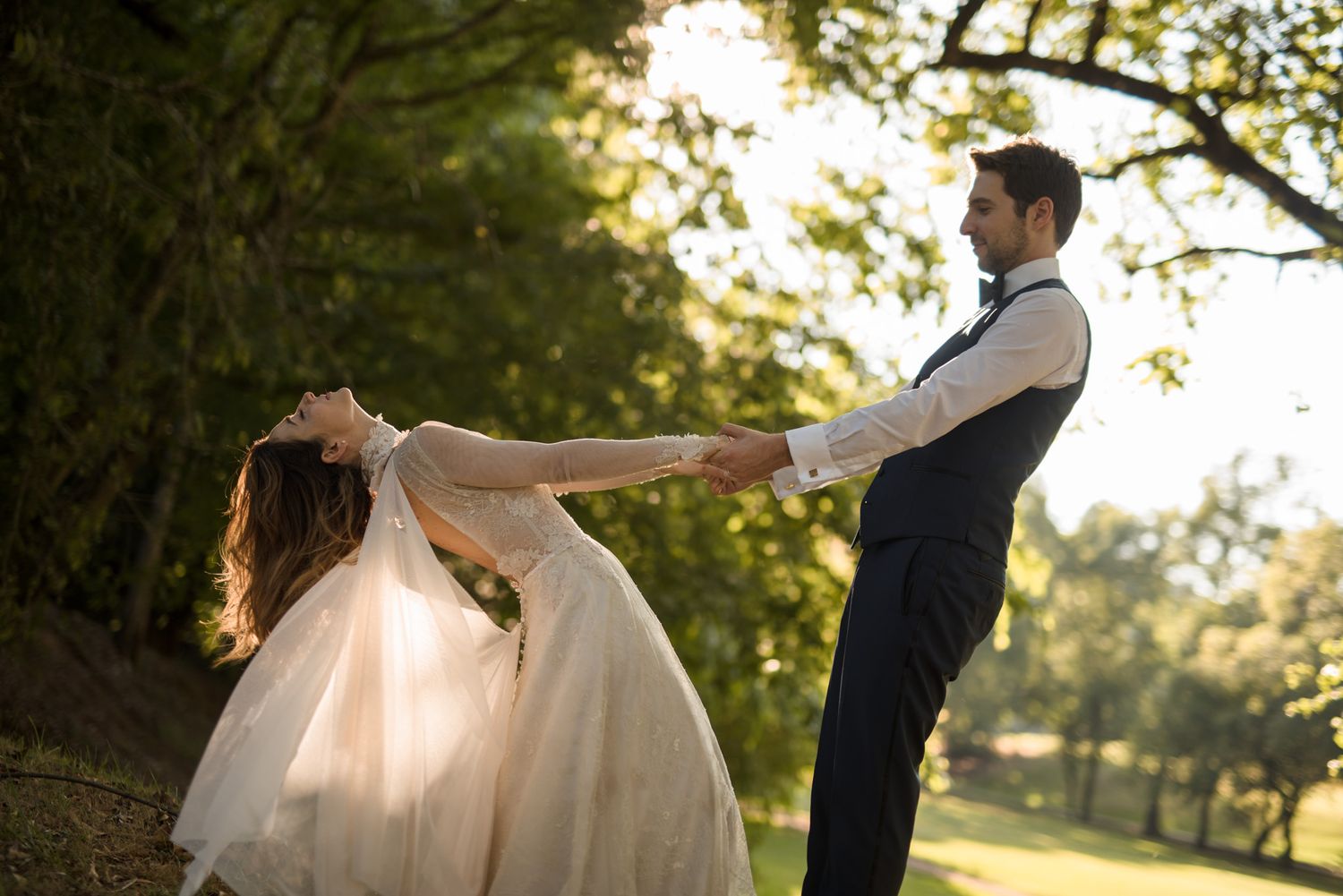 A bride and groom dance together in a romantic outdoor setting during golden hour at their wedding.