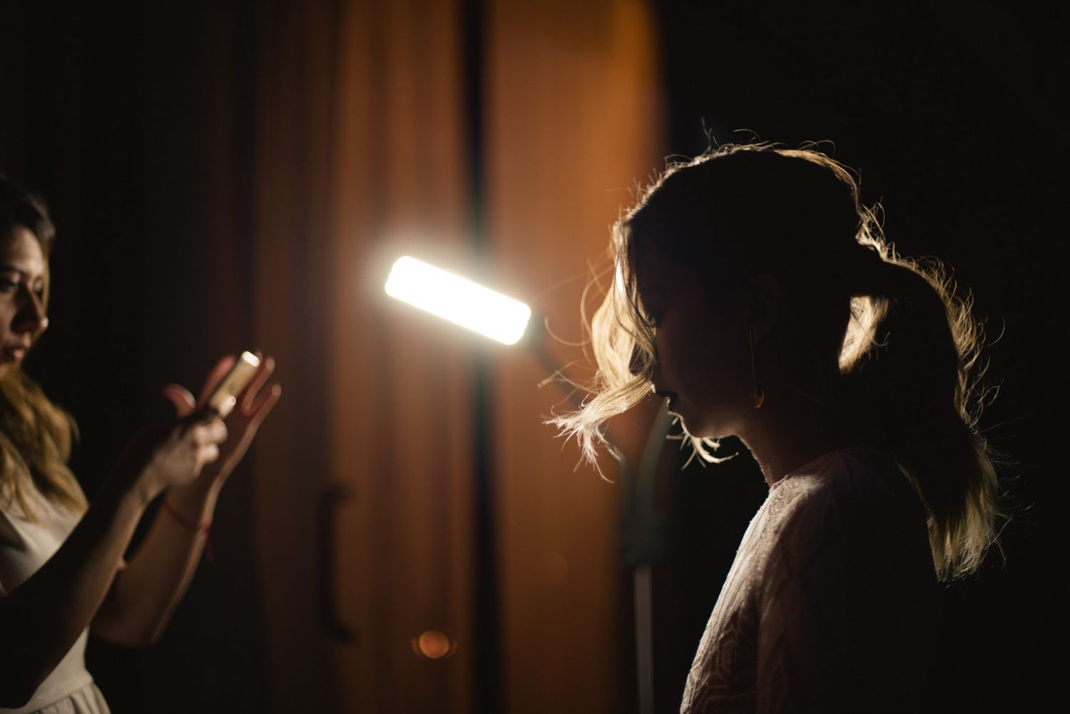 People stand in a dark space with dramatic lighting as light glows from a phone screen.