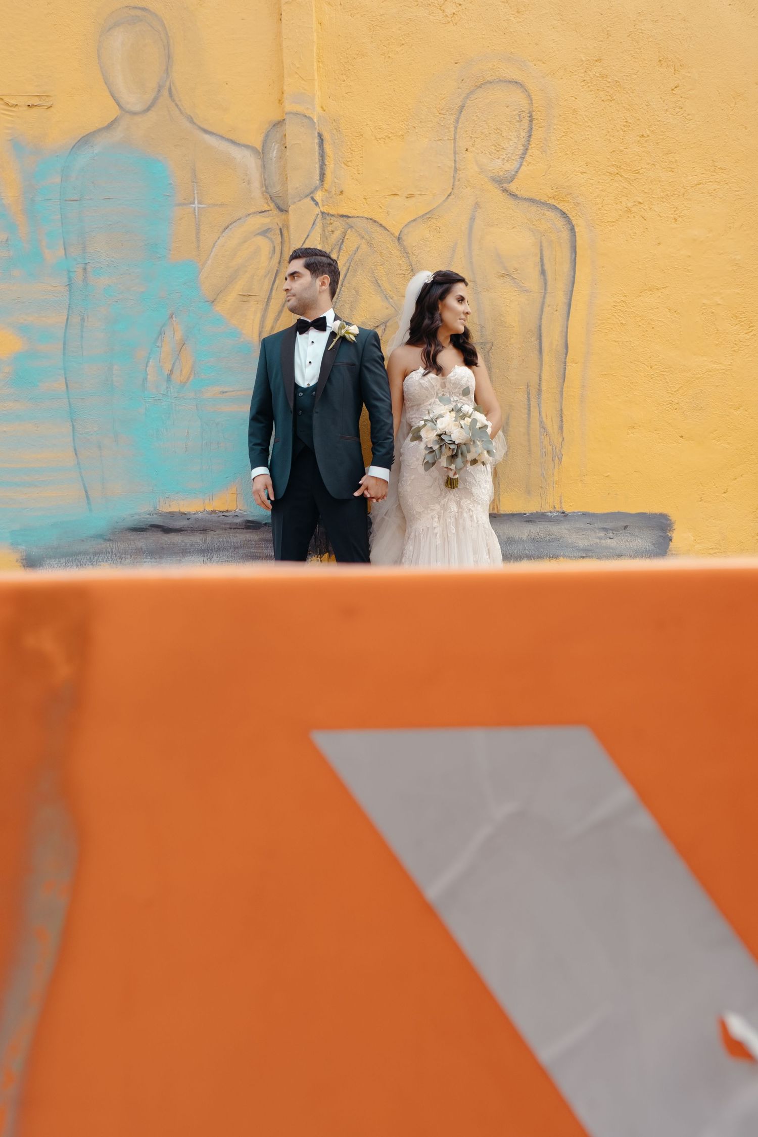 Modern wedding portrait against yellow wall with artistic silhouette mural.