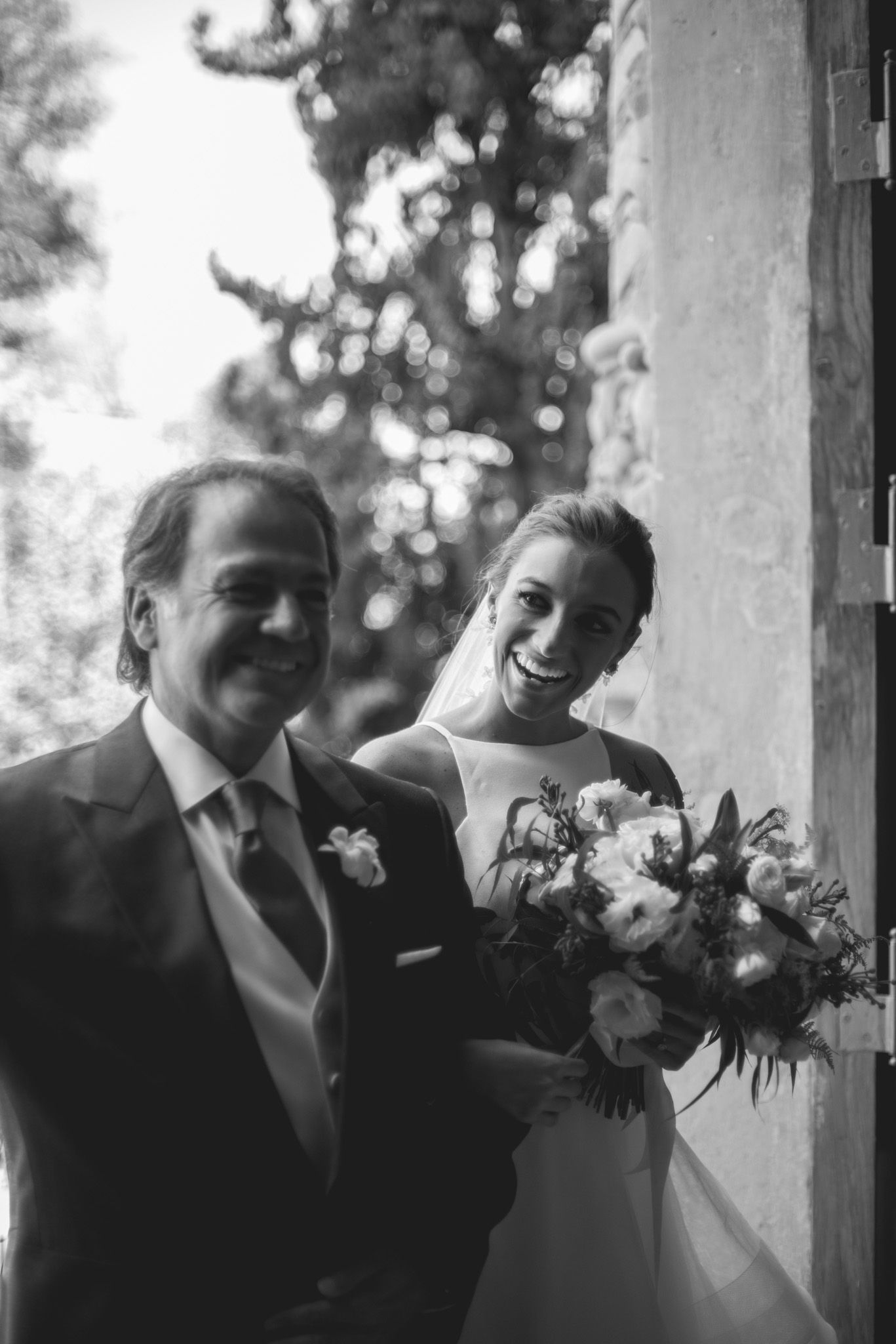 A black and white wedding portrait showing a couple standing together with a floral bouquet.