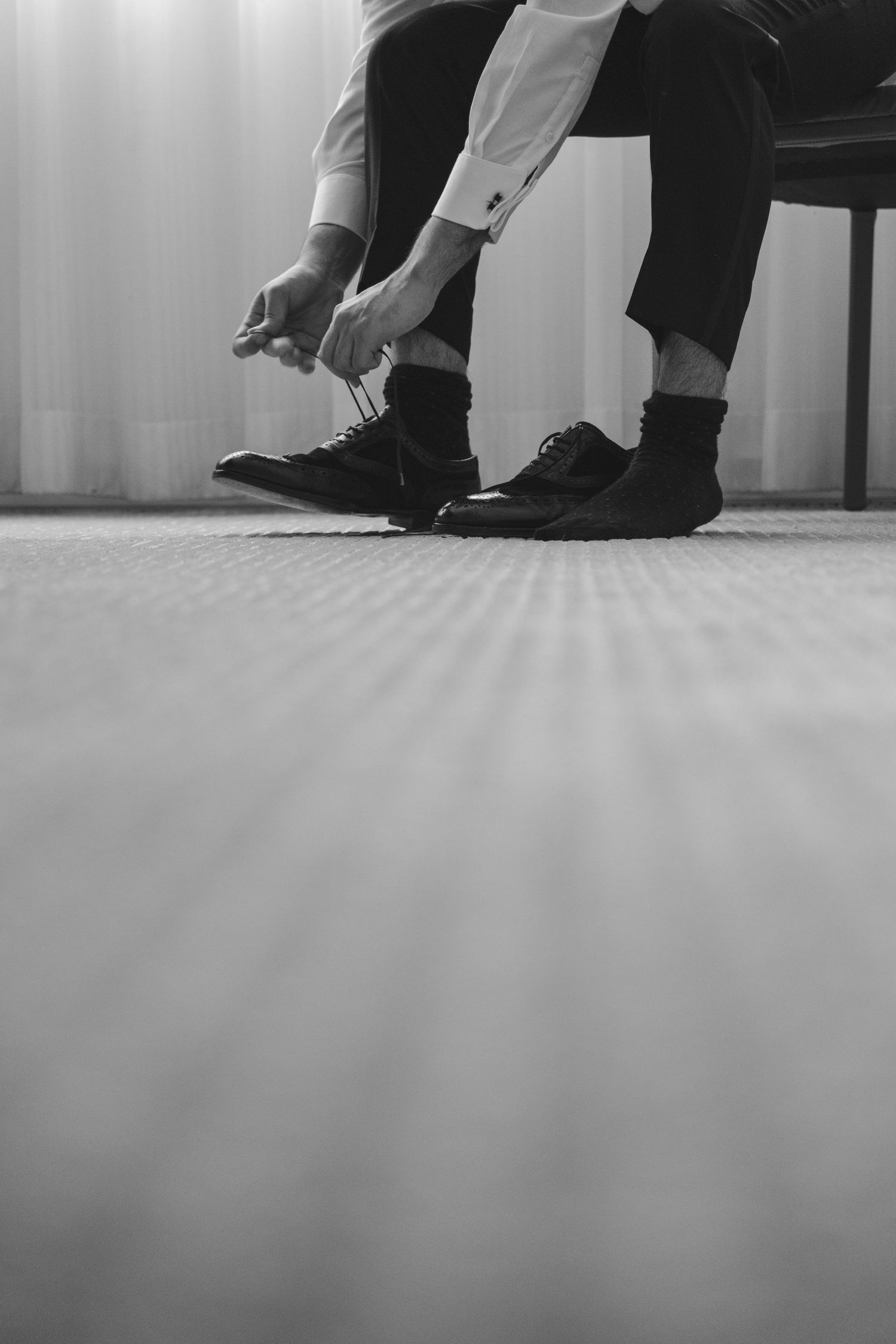 Low angle view of someone tying formal black dress shoes on wooden floor.