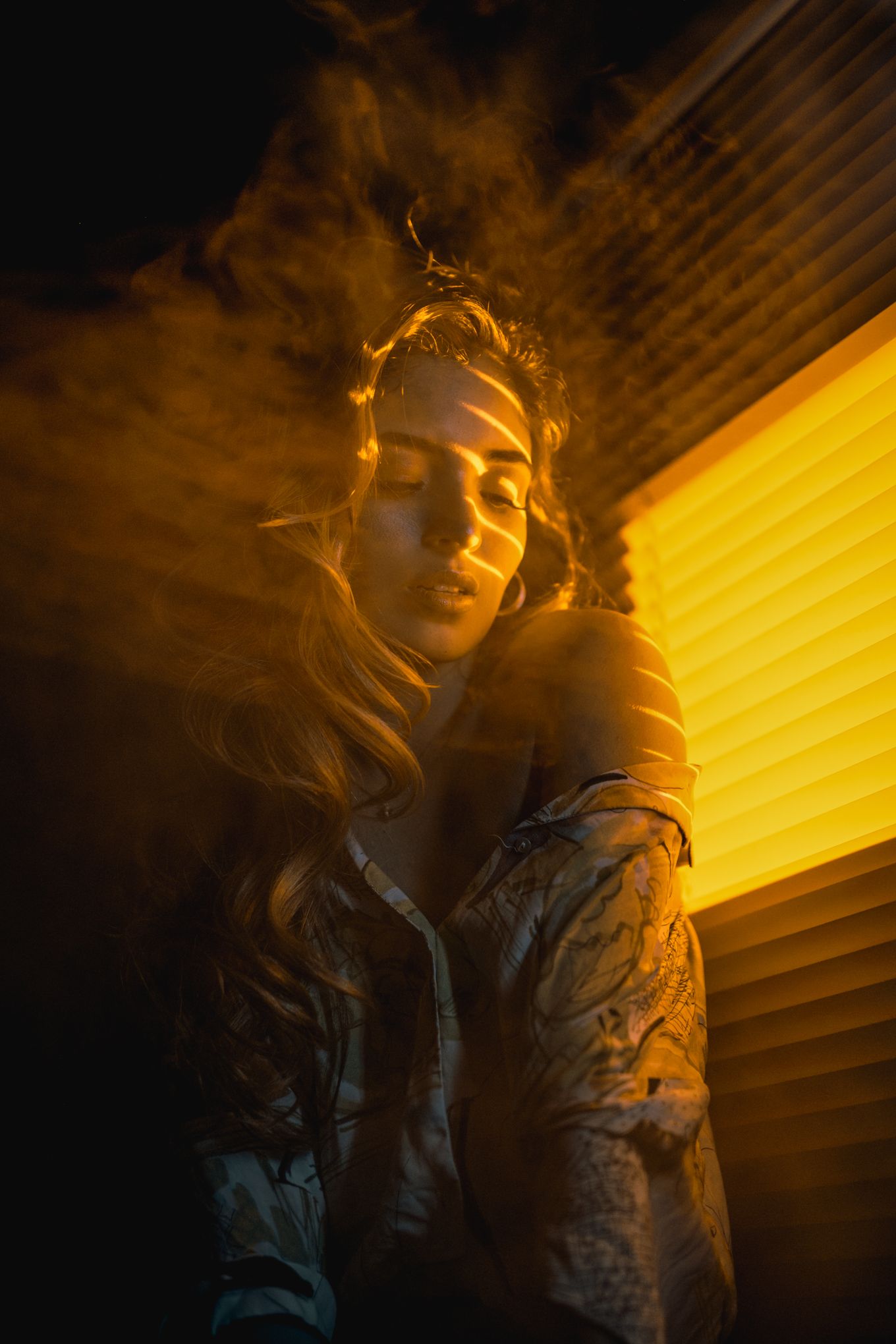 Artistic portrait with golden light streaming through window blinds creating moody atmosphere.