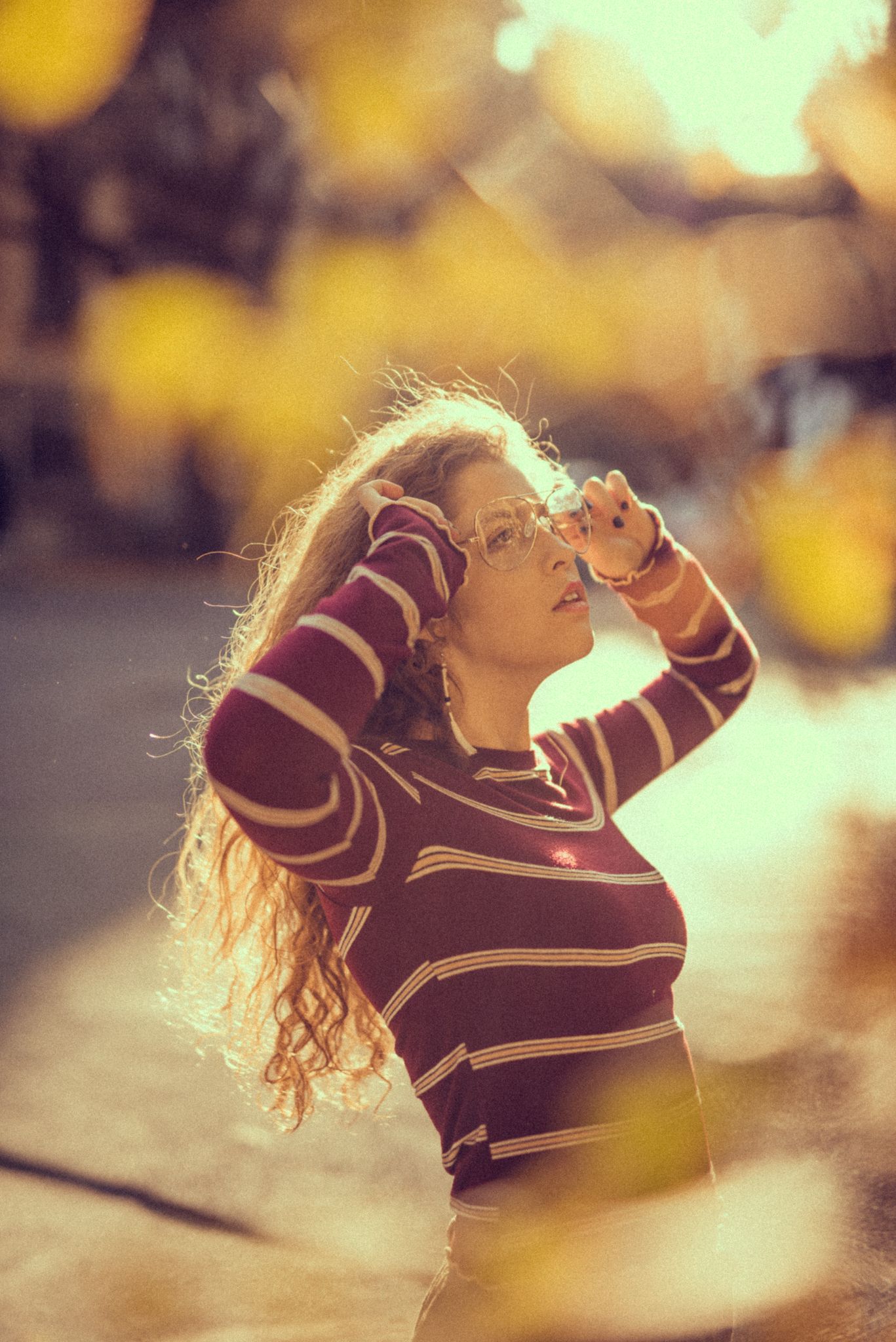 Person in striped sweater poses outdoors with backlit golden bokeh effect.
