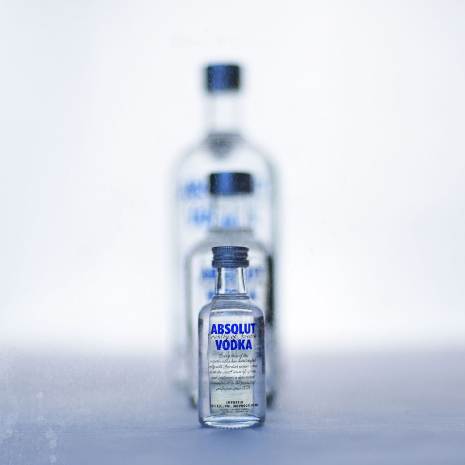 Three identical Absolut vodka bottles fade into a soft white background with decreasing clarity.