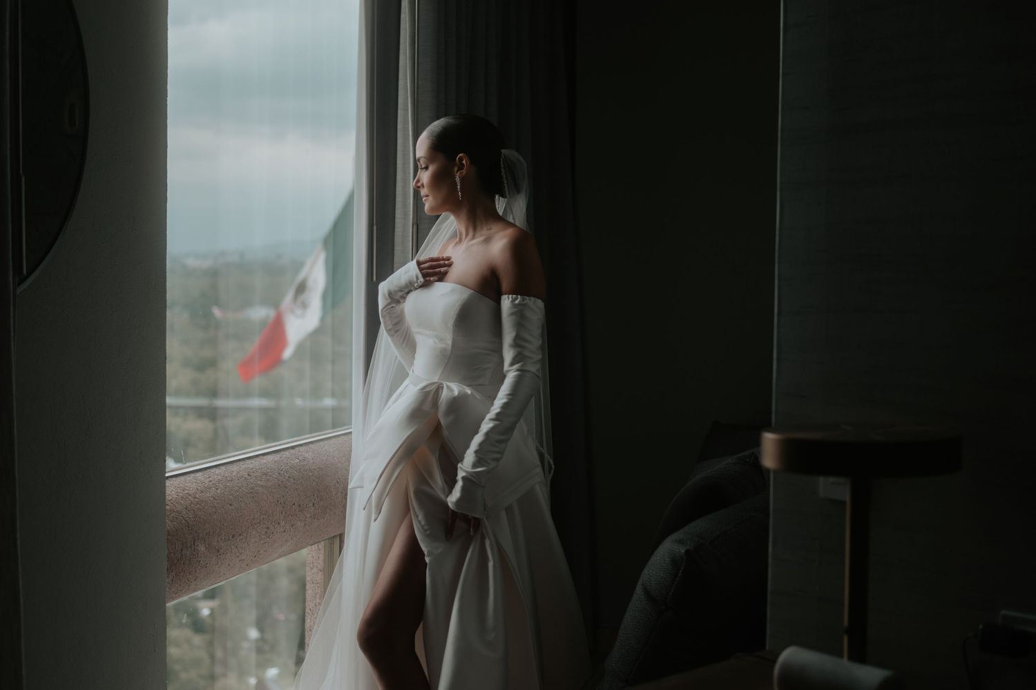Elegant bridal portrait near window showing flowing white dress and long gloves.