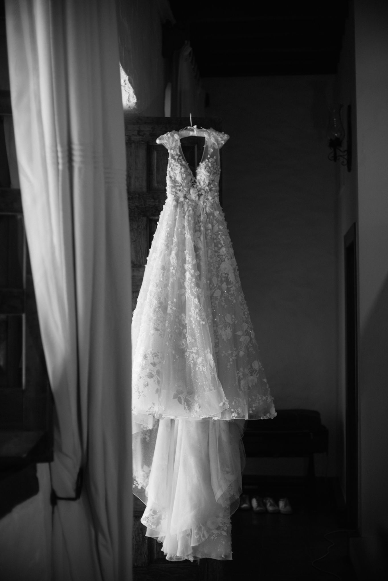Elegant lace wedding dress hanging in doorway, captured in black and white.