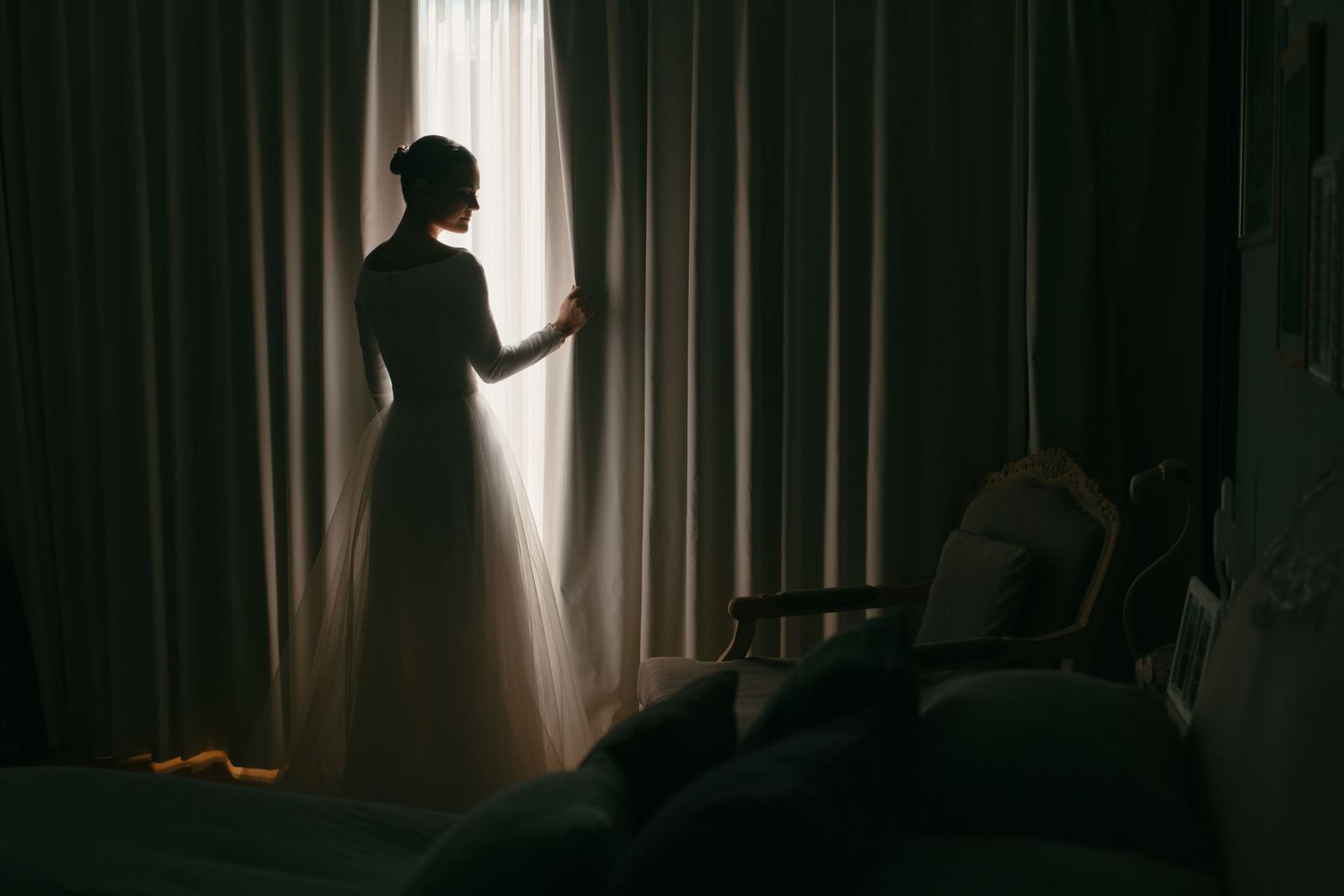 Dramatic silhouette of a person standing by window curtains in morning light.