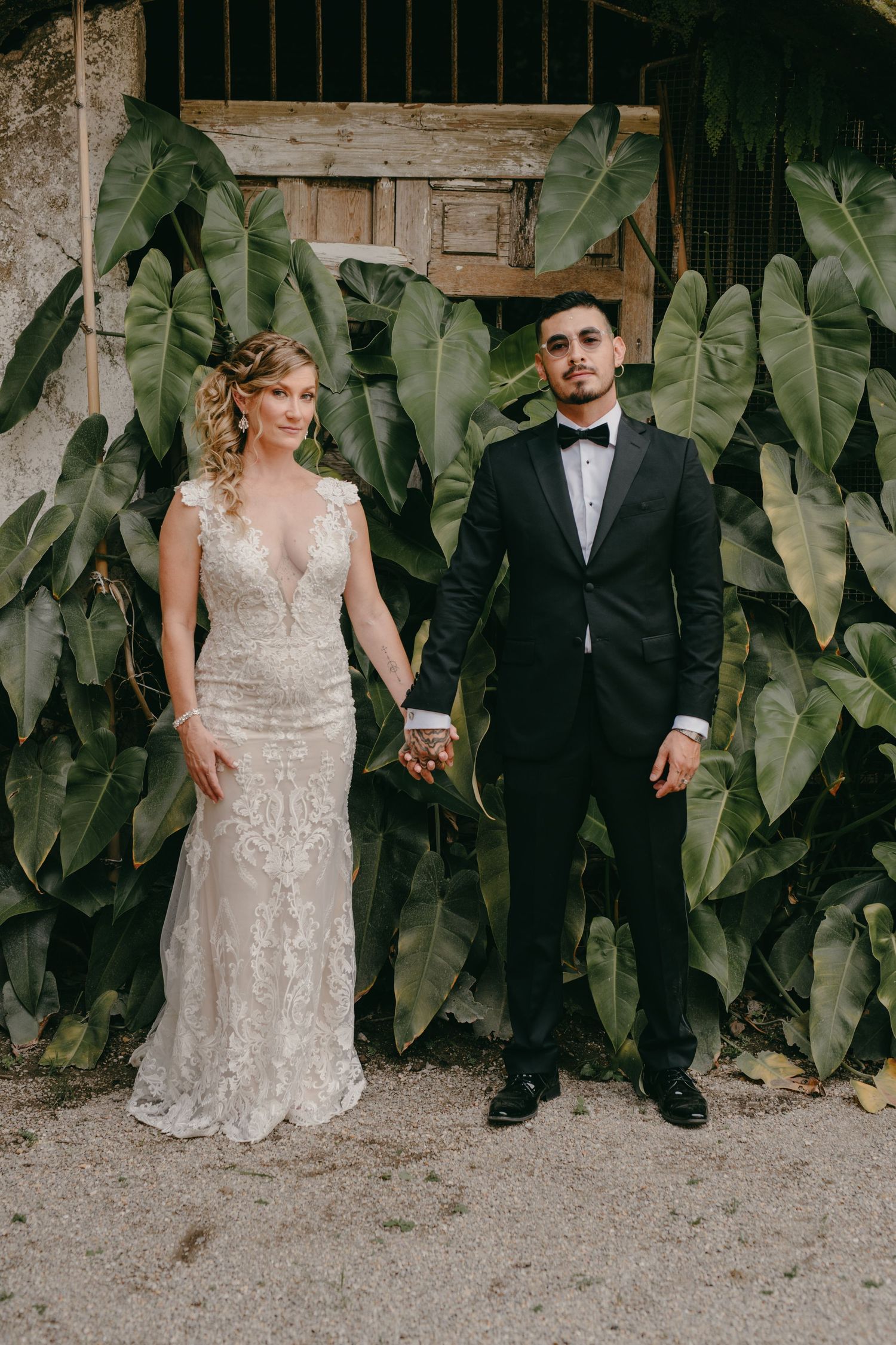 Wedding couple poses against lush tropical foliage backdrop.