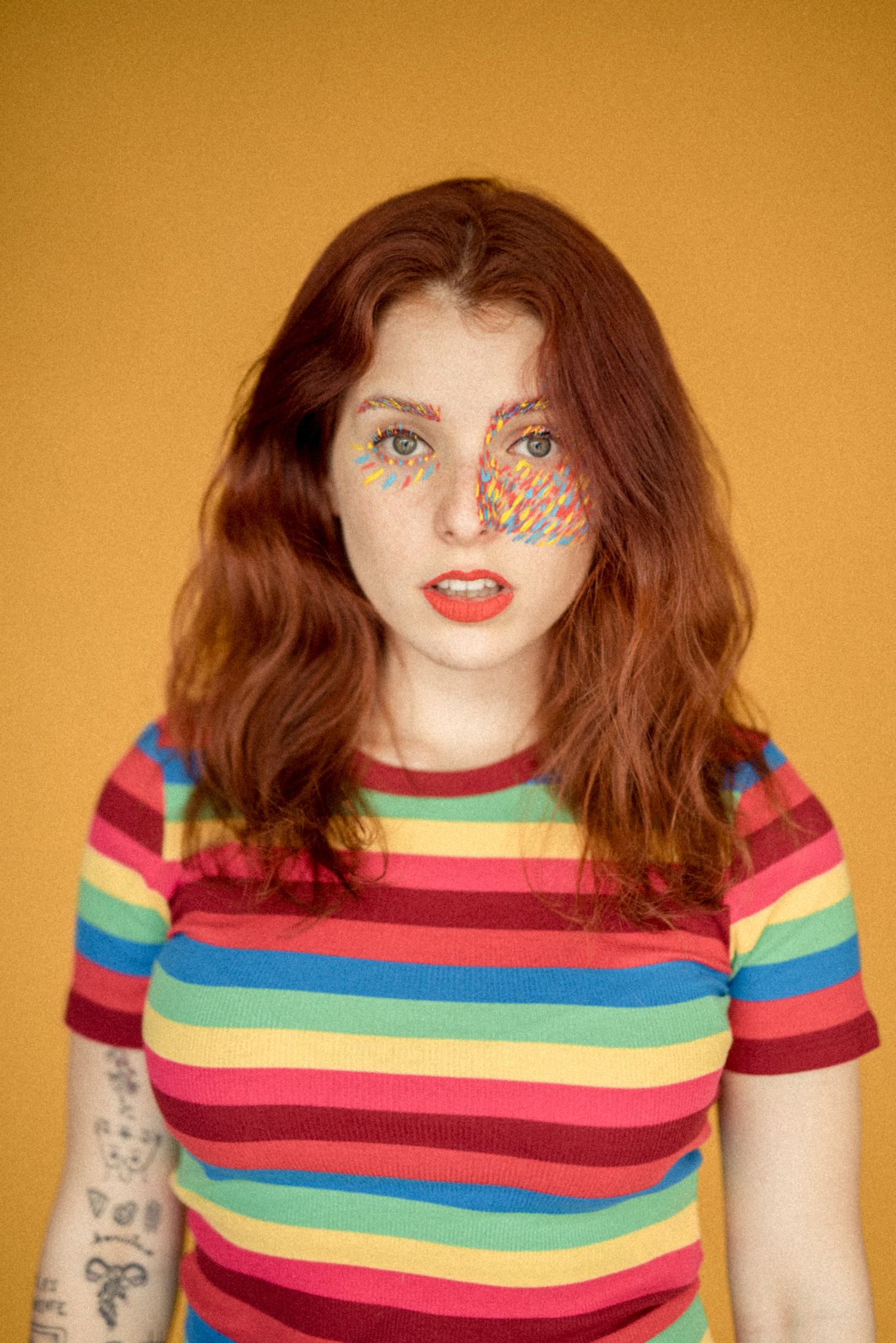 Creative beauty portrait with rainbow glitter makeup against orange background.