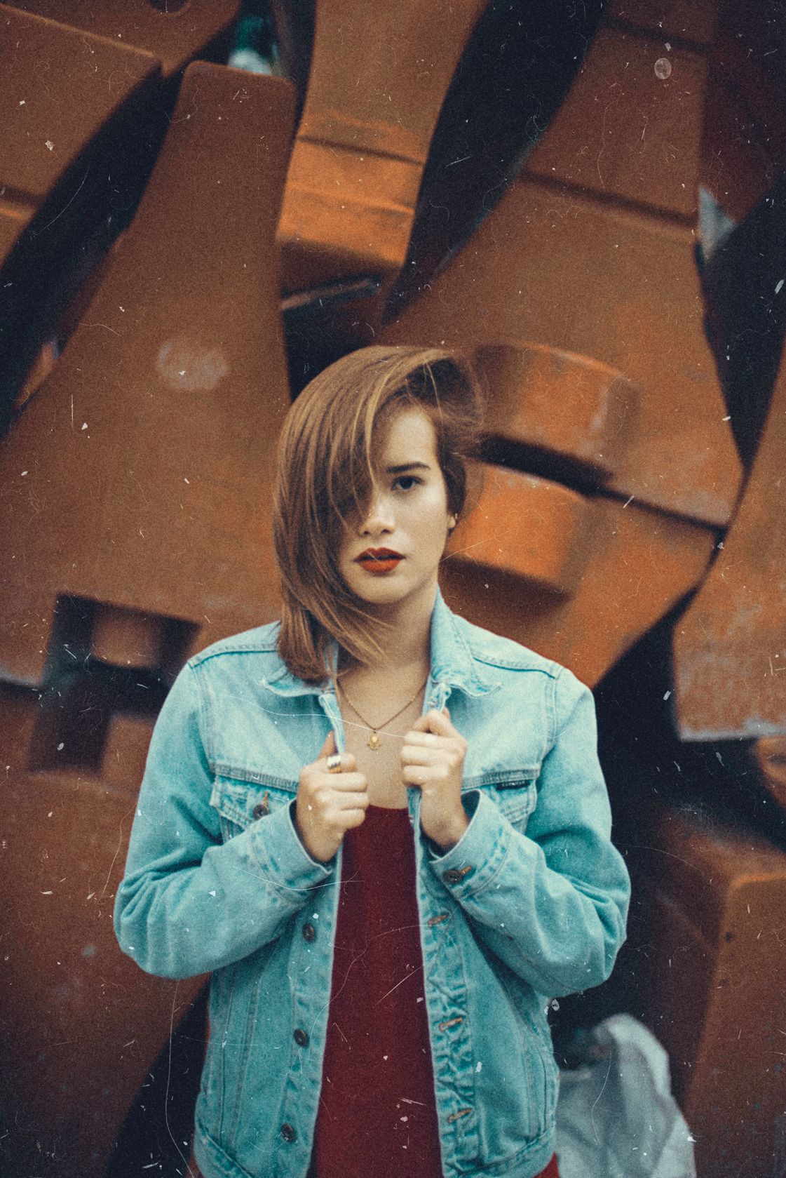 Person in denim jacket against industrial backdrop with dramatic lighting.