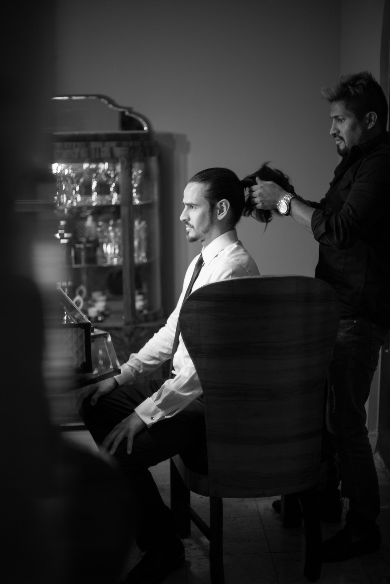 Black and white portrait of stylist working on a client seated in chair in an elegantly lit room.