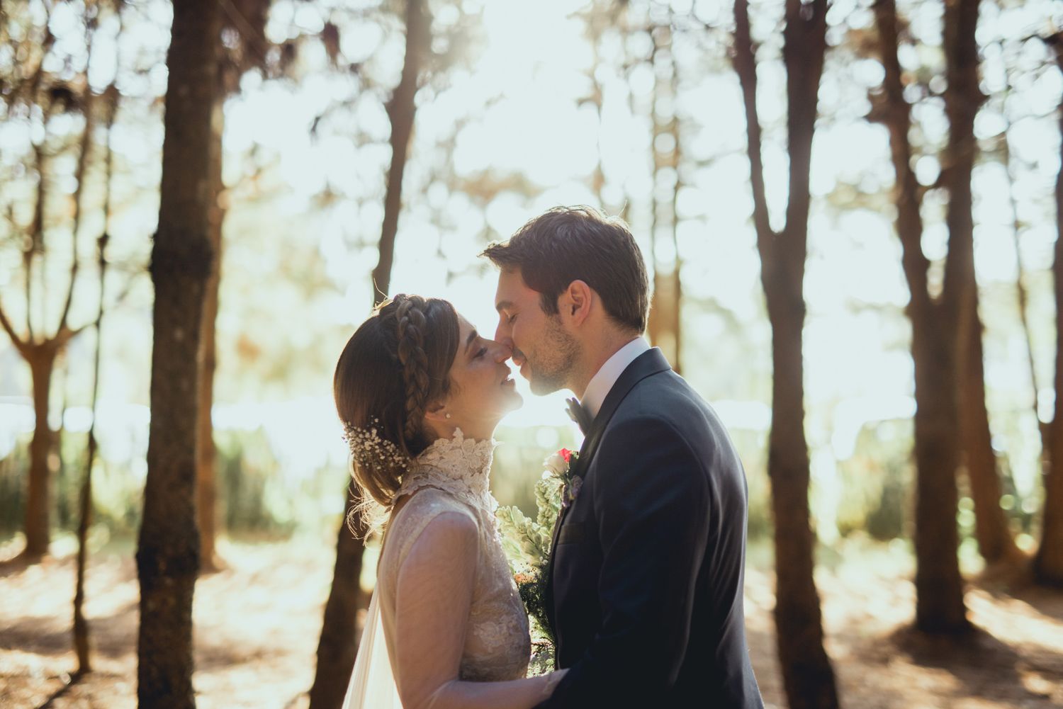 A loving couple shares a romantic moment in a sun-dappled forest setting during their wedding celebration.