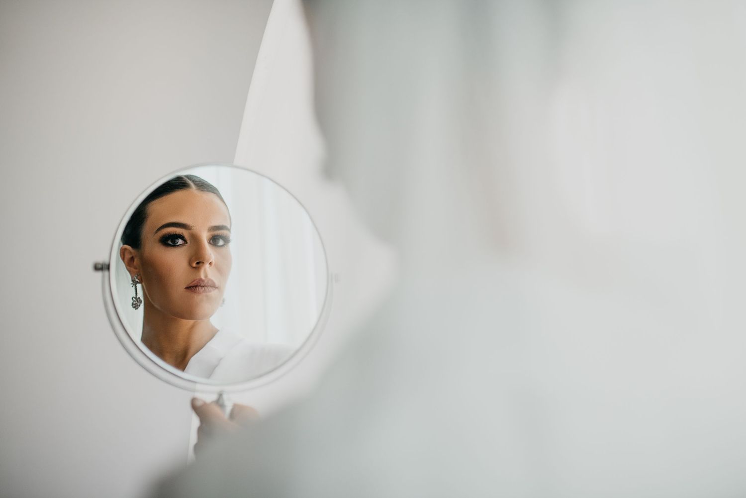 A reflection in a round mirror set against a white wall captures a poised figure in elegant formal attire.