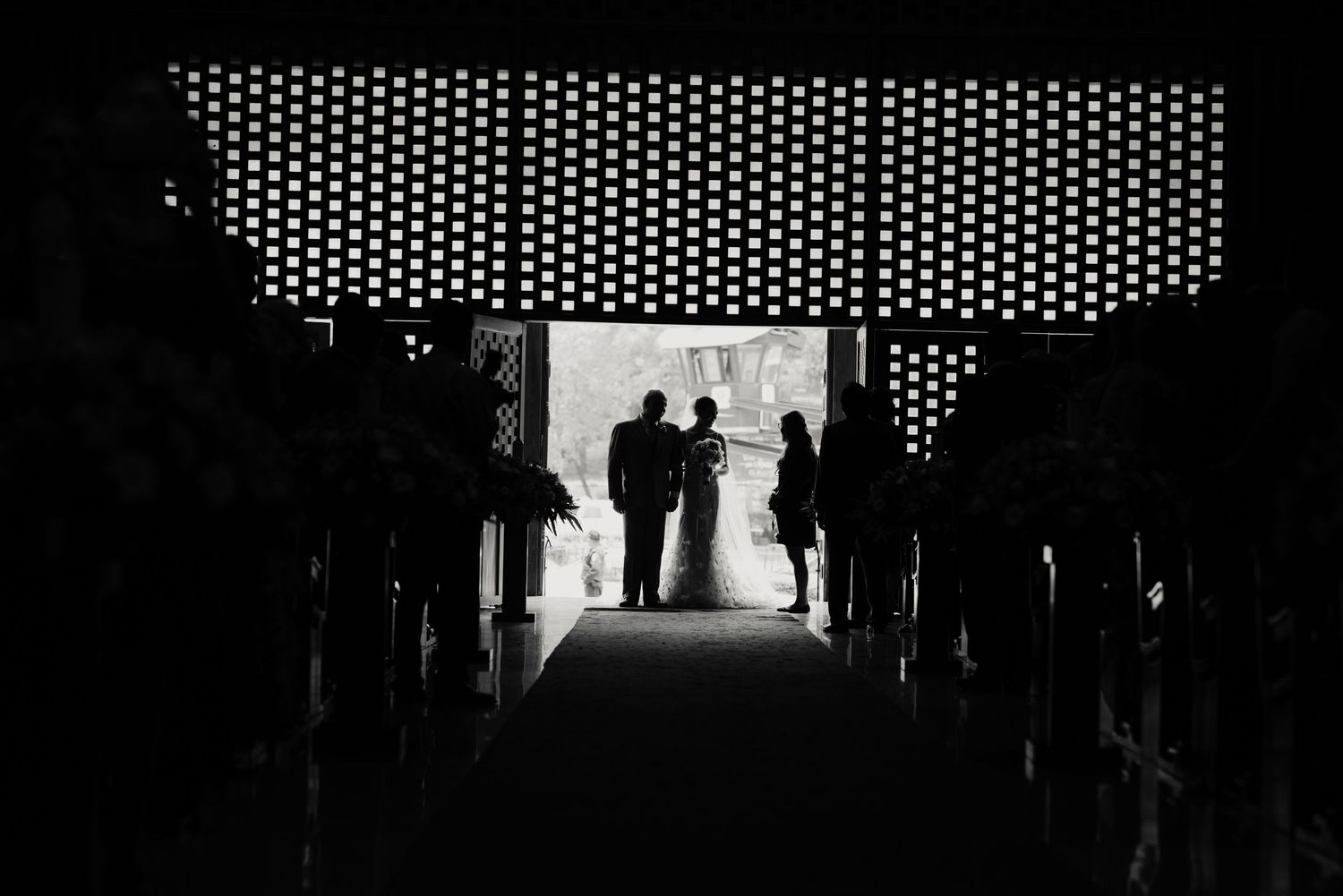 Silhouetted figures seen through a tunnel-like hallway entrance with perforated metal ceiling above.
