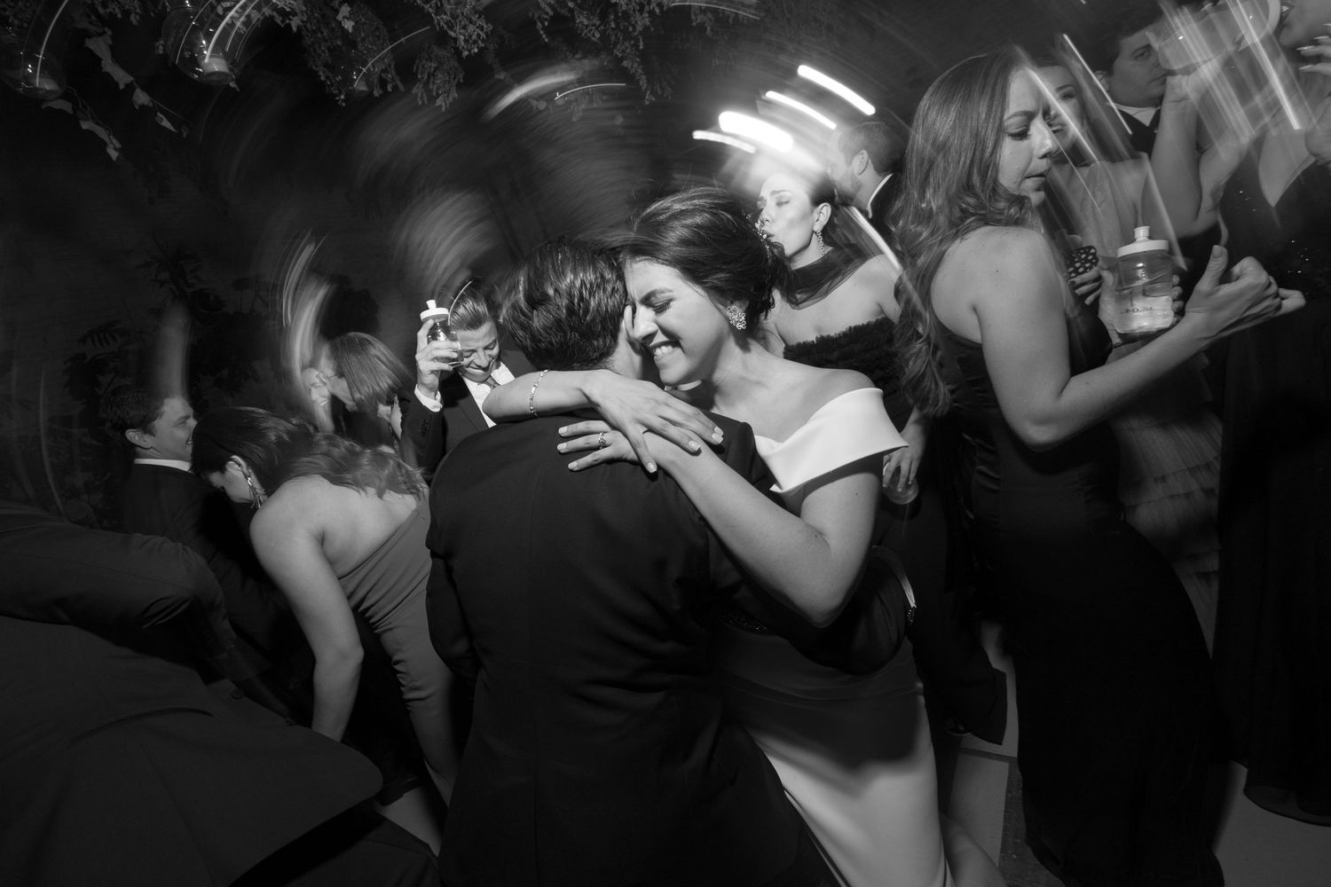 A couple embraces while slow dancing at a nightclub as other guests dance in the background.