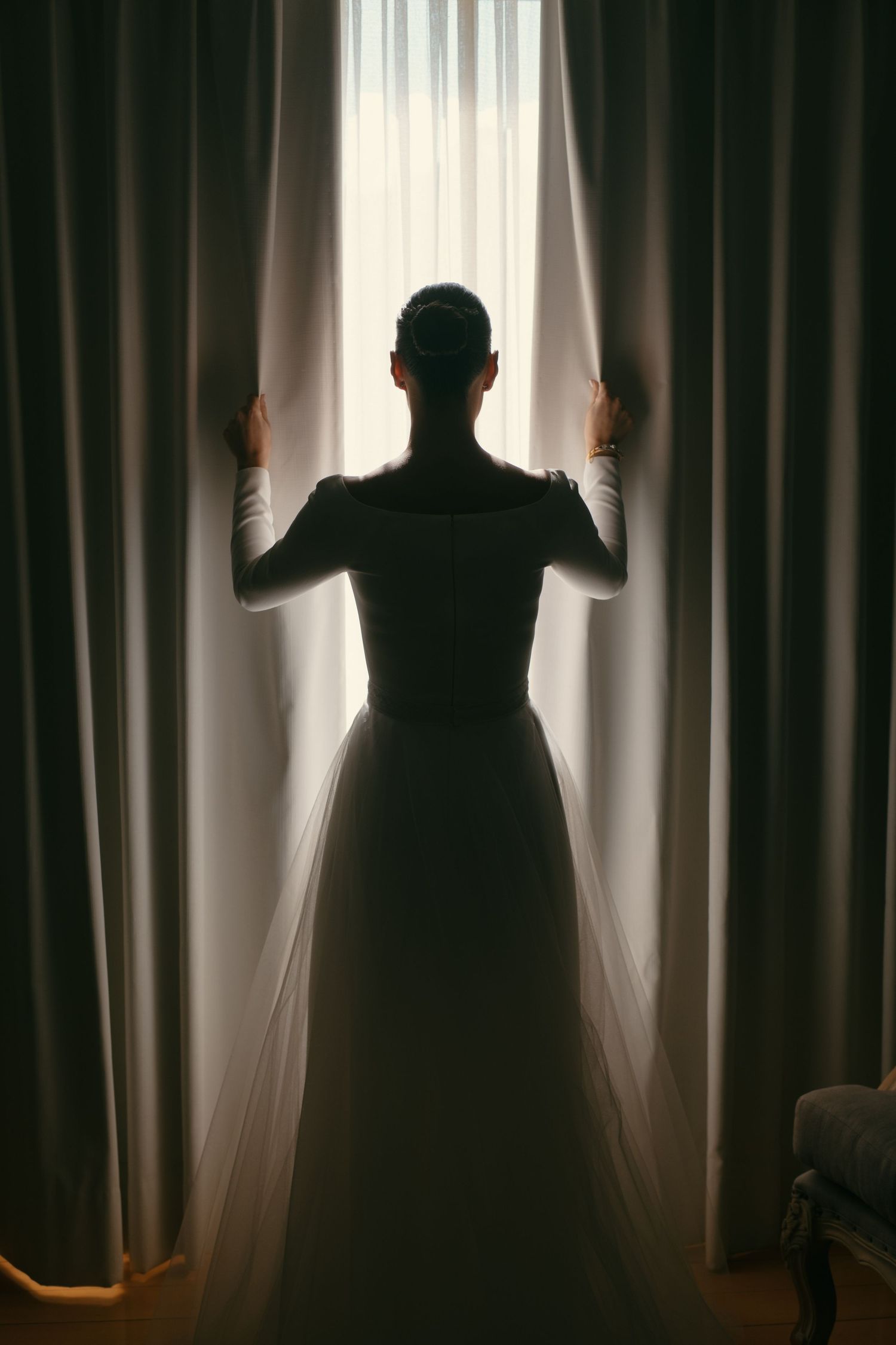 Silhouetted figure in a flowing dress stands before a window with dramatic curtains creating a backlit ethereal effect.