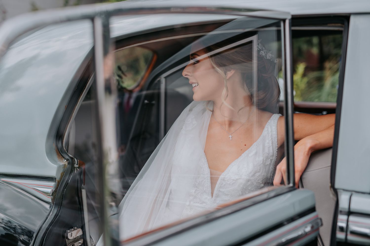 Classic vintage car scene with elegant bride in white veil seated in luxurious black vehicle.