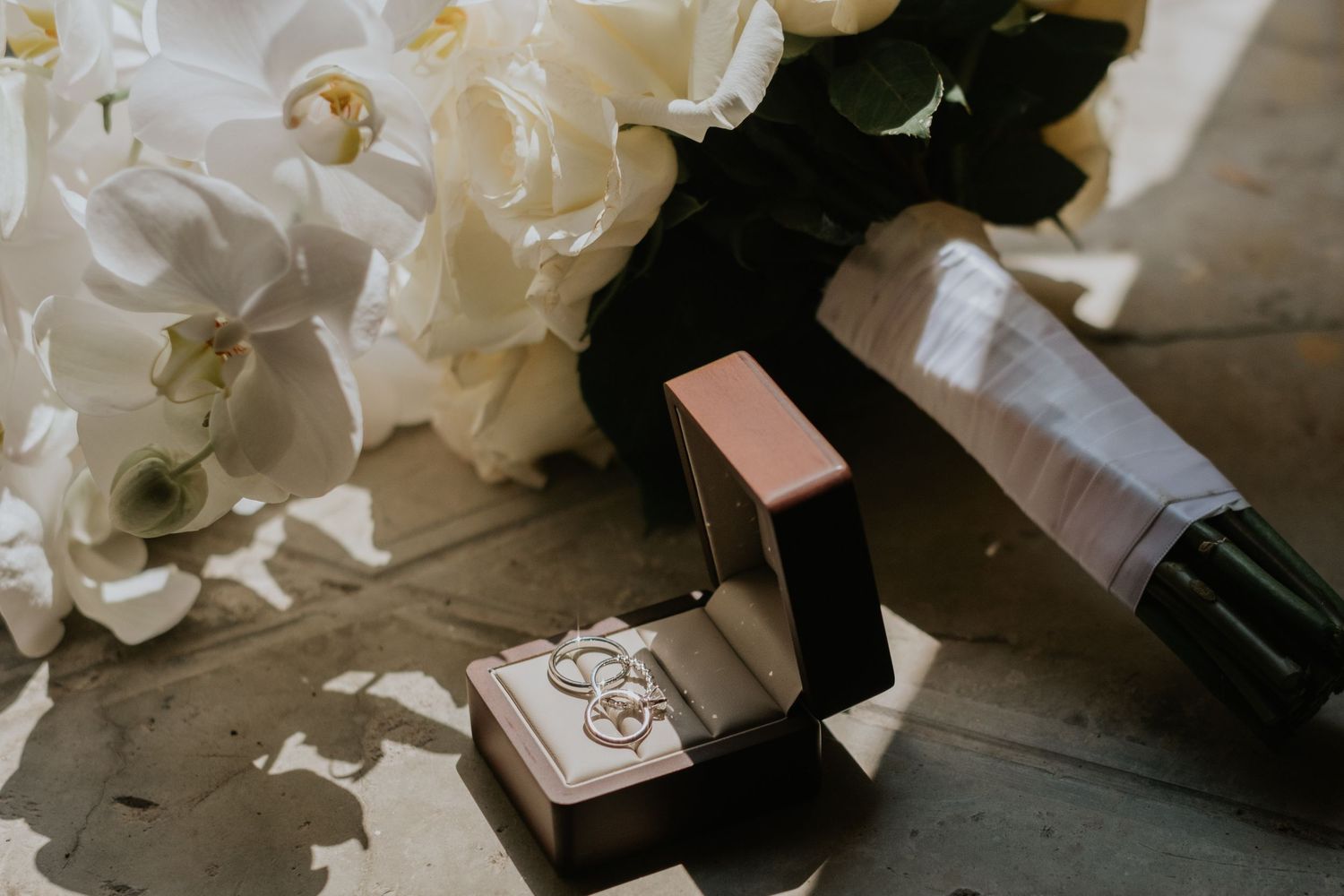 Wedding details with white orchids and velvet ring box on rustic surface.