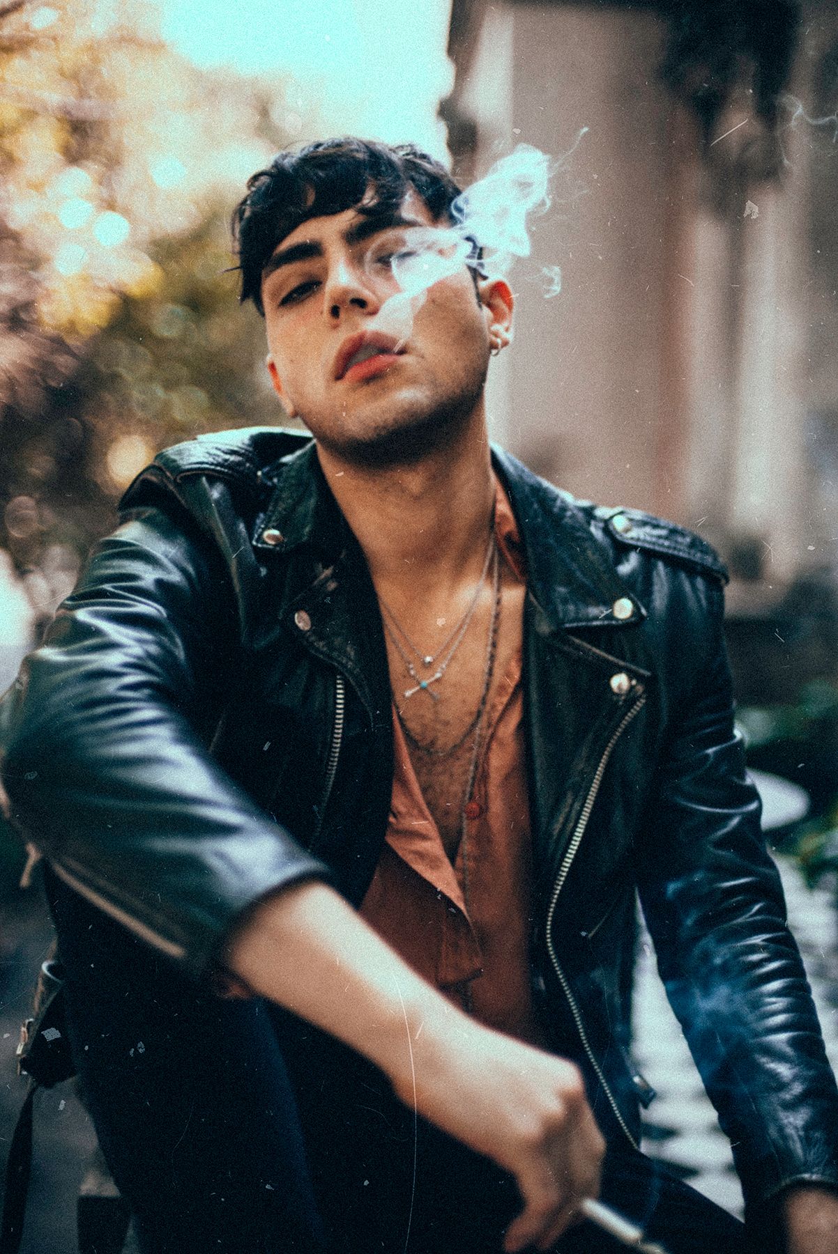 Stylish portrait of person in leather jacket exhaling smoke outdoors.