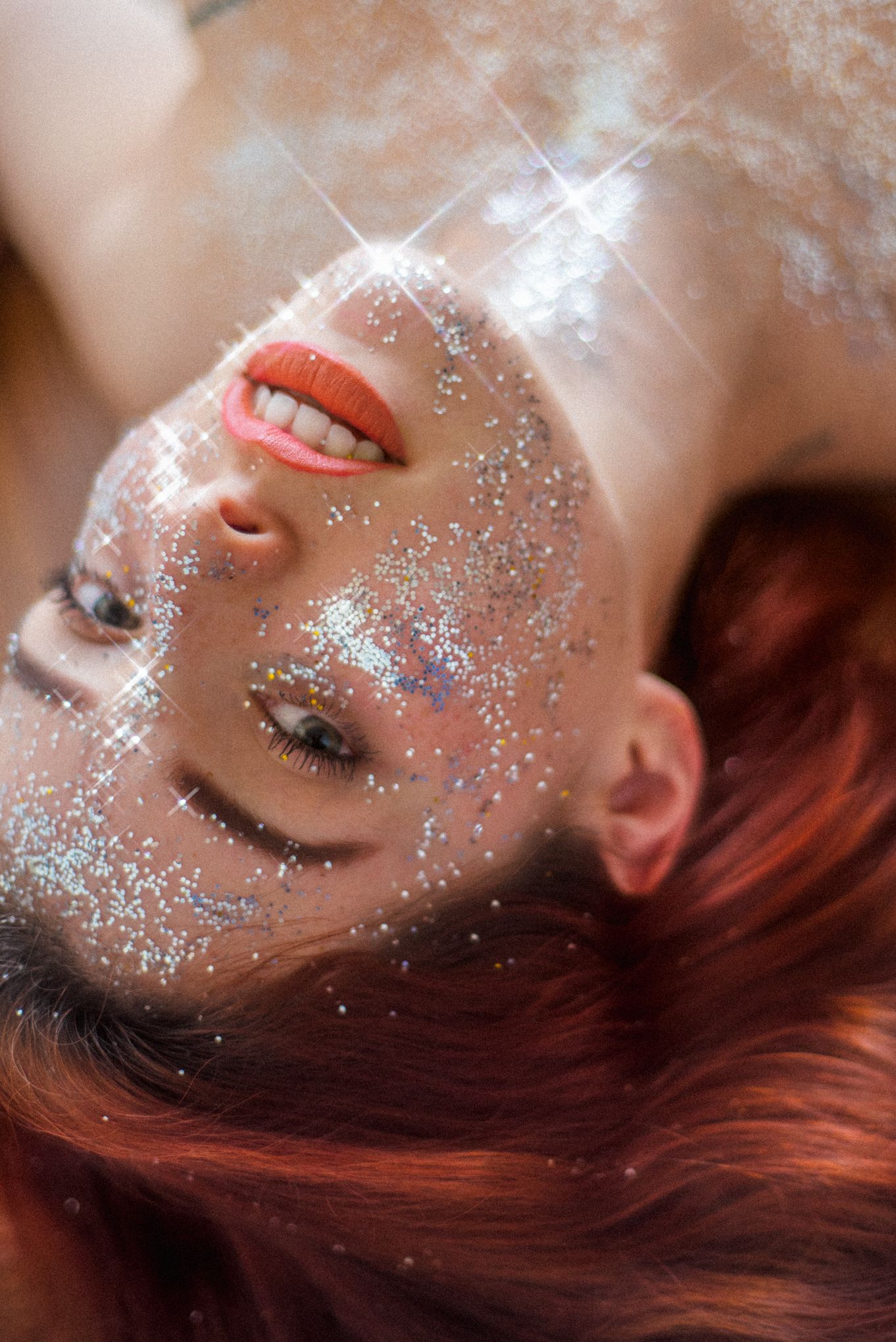 Close-up beauty portrait with sparkly glitter makeup and red lipstick against soft background.