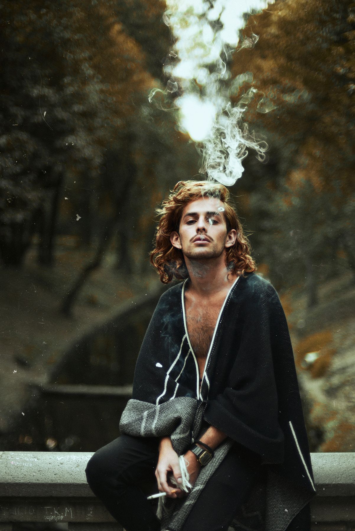 Person in black coat smoking while sitting outdoors in autumn setting.